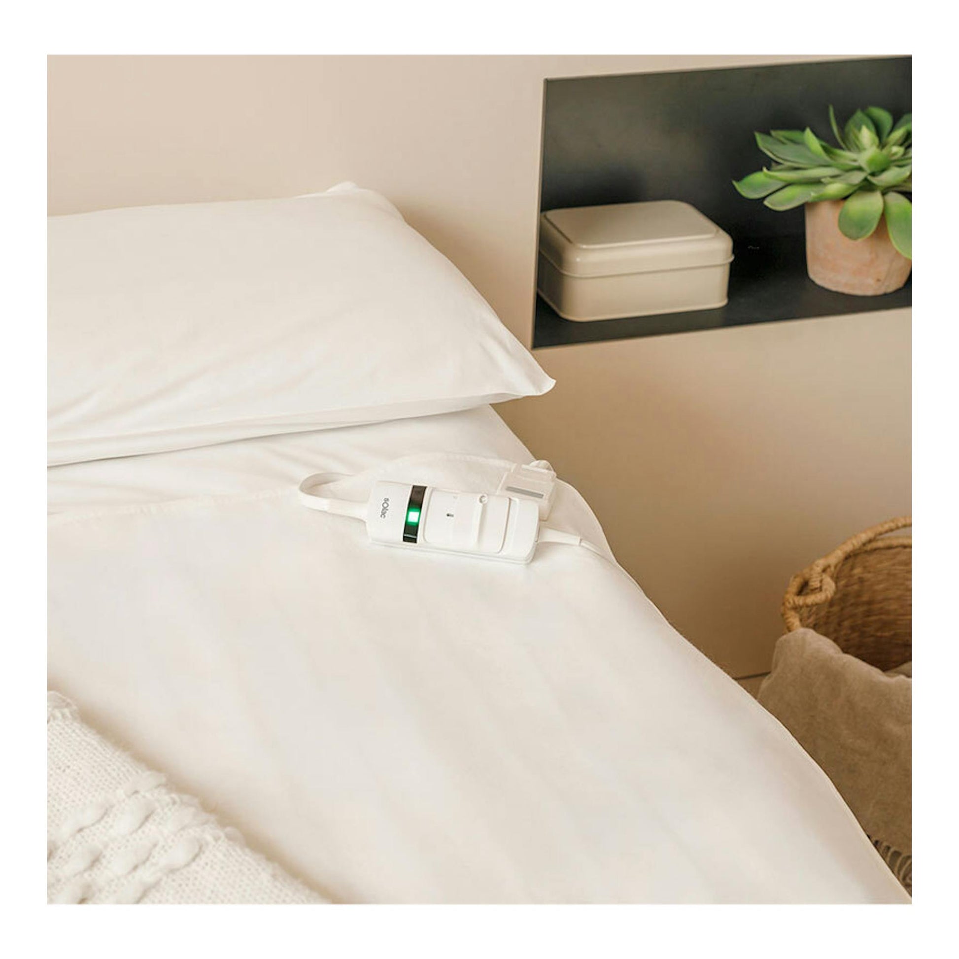 Calientacamas Solac Denmark CT8704 blanco sobre una cama con sábanas blancas y mando con luz verde.