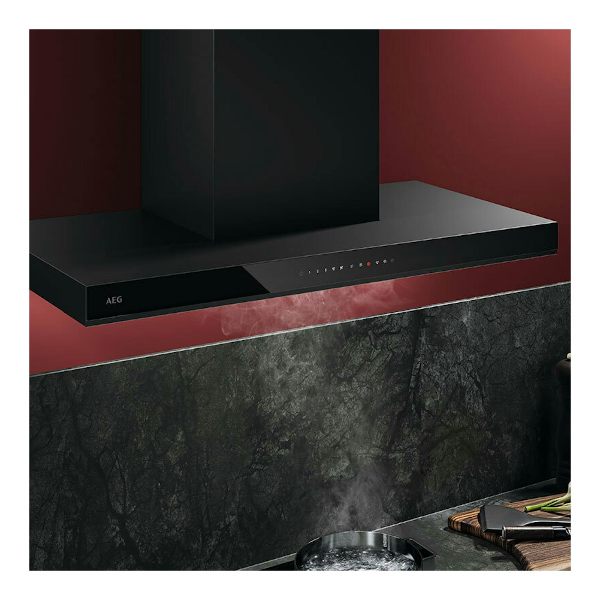 Campana decorativa AEG GB87D91CB negra, vista frontal en ángulo, sobre pared roja.