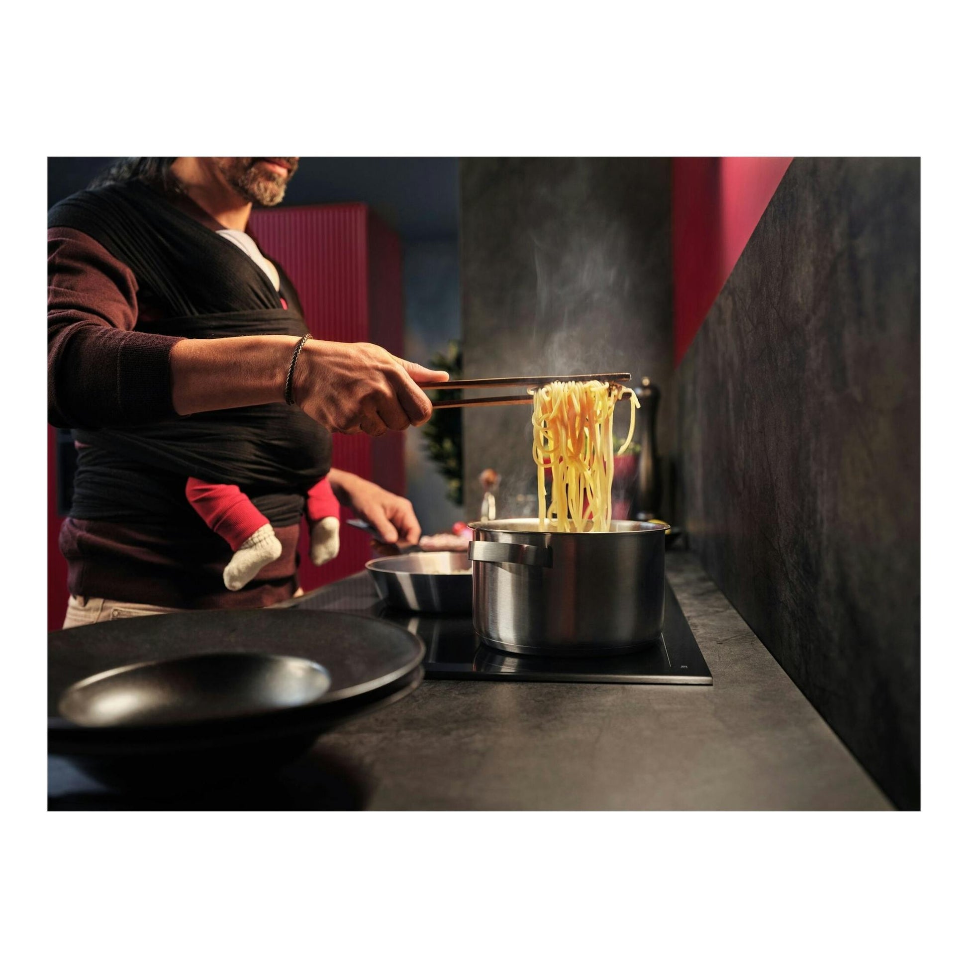 Persona cocinando pasta en una placa de inducción negra, con vapor sobre una olla de acero.