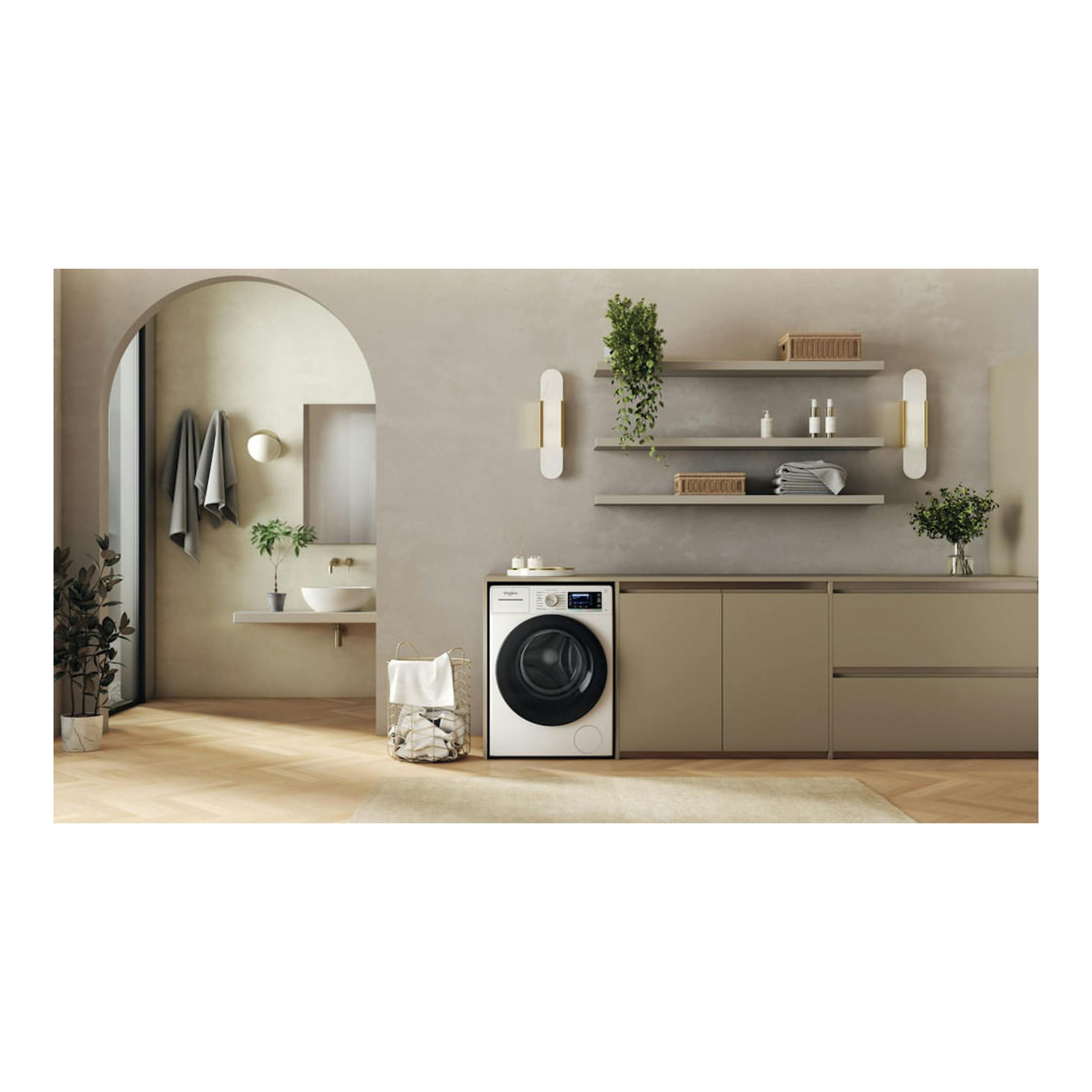 Lavadora Whirlpool blanca de carga frontal, vista frontal, en lavandería moderna con muebles beige y estantes.