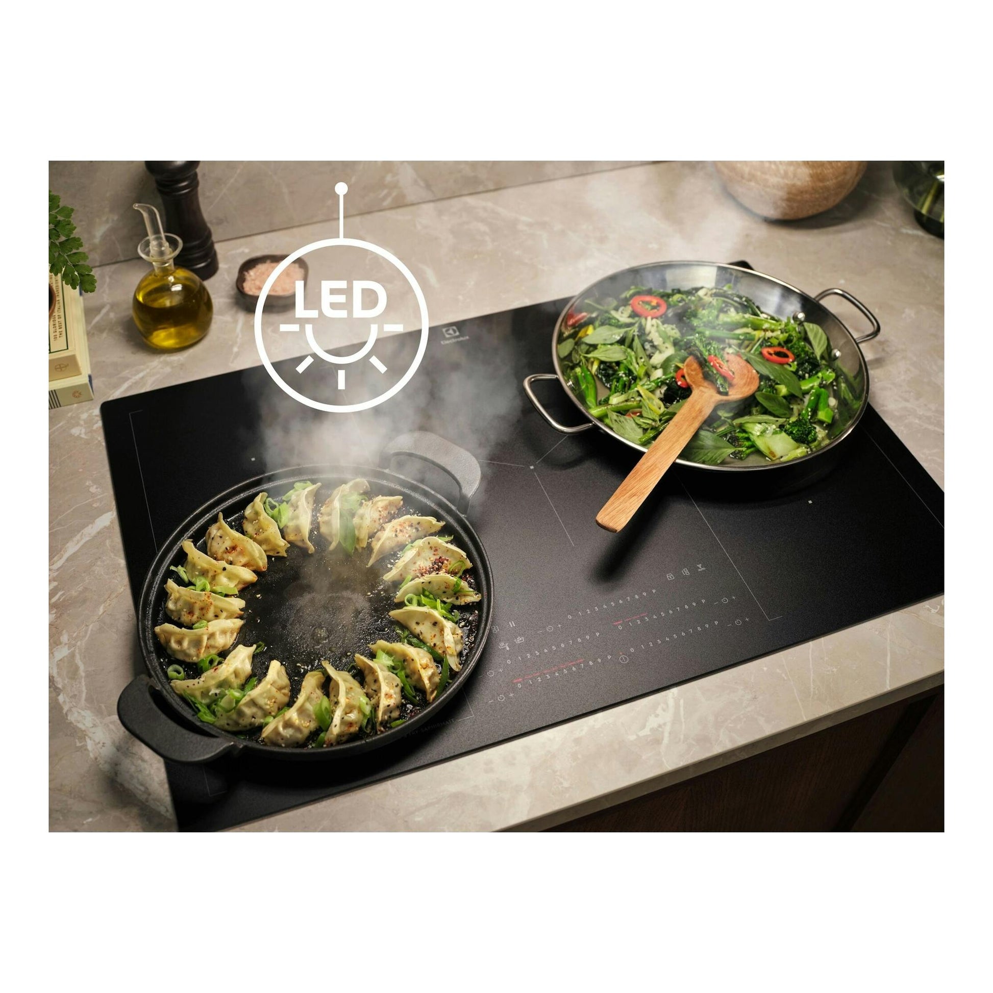 Plano cenital de cocina de inducción Electrolux negra con dos sartenes, vapor y icono LED.