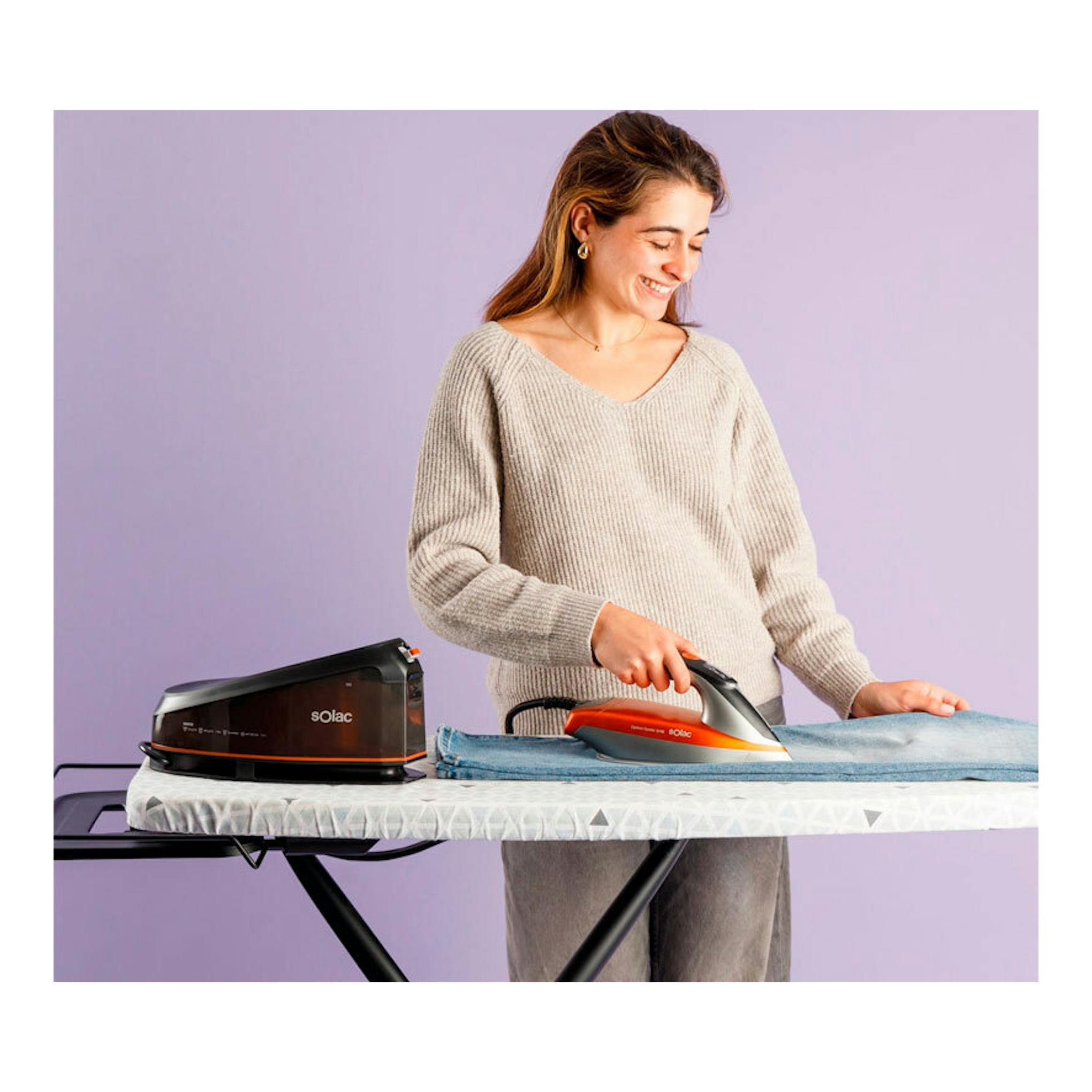 Centro de planchado Solac CPB6110 negro y naranja sobre tabla de planchar, usado por una mujer.