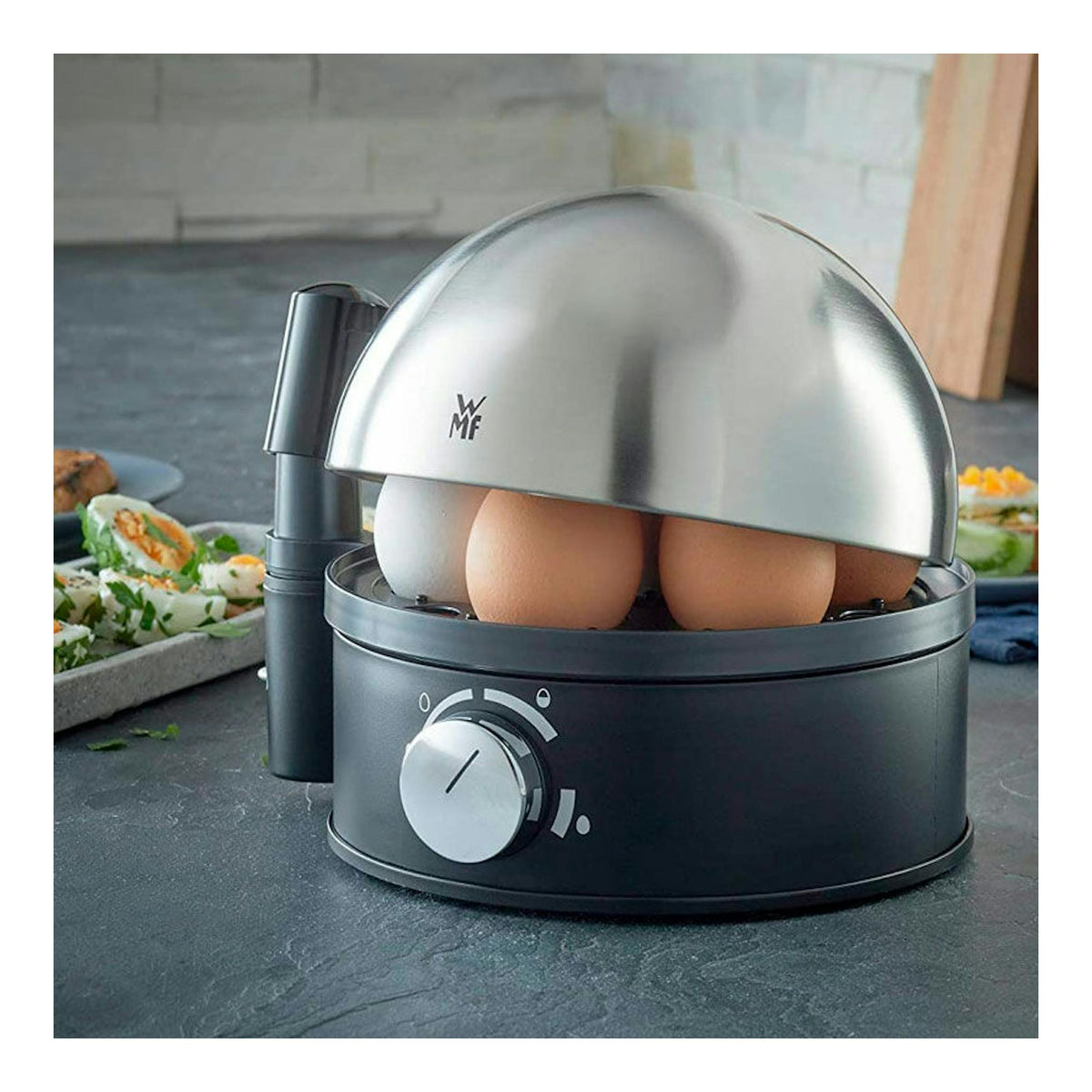 Cocedora de huevos WMF STELIO negra y plateada, vista frontal con tapa abatible abierta y huevos dentro.