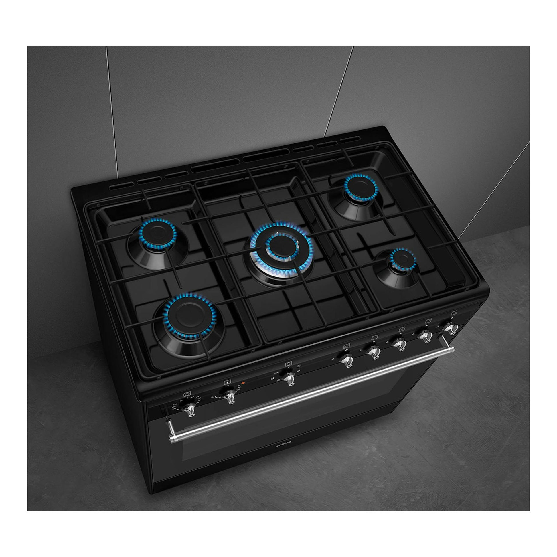Cocina de gas Smeg CX91GMBL negra, vista cenital inclinada, 5 quemadores con llamas azules y horno.