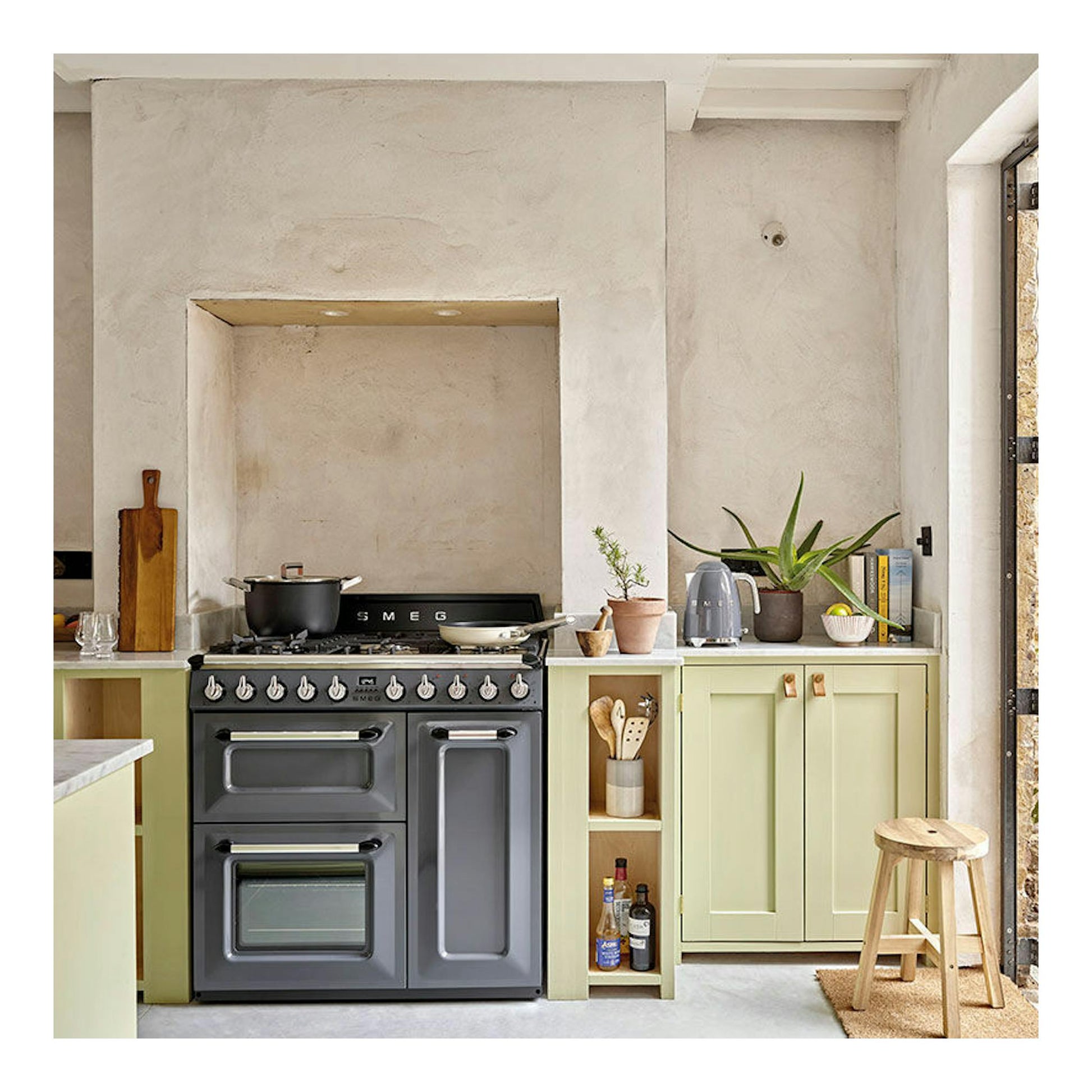 Cocina Smeg TR103GR gris, vista frontal en una cocina con encimera, plantas y taburete.