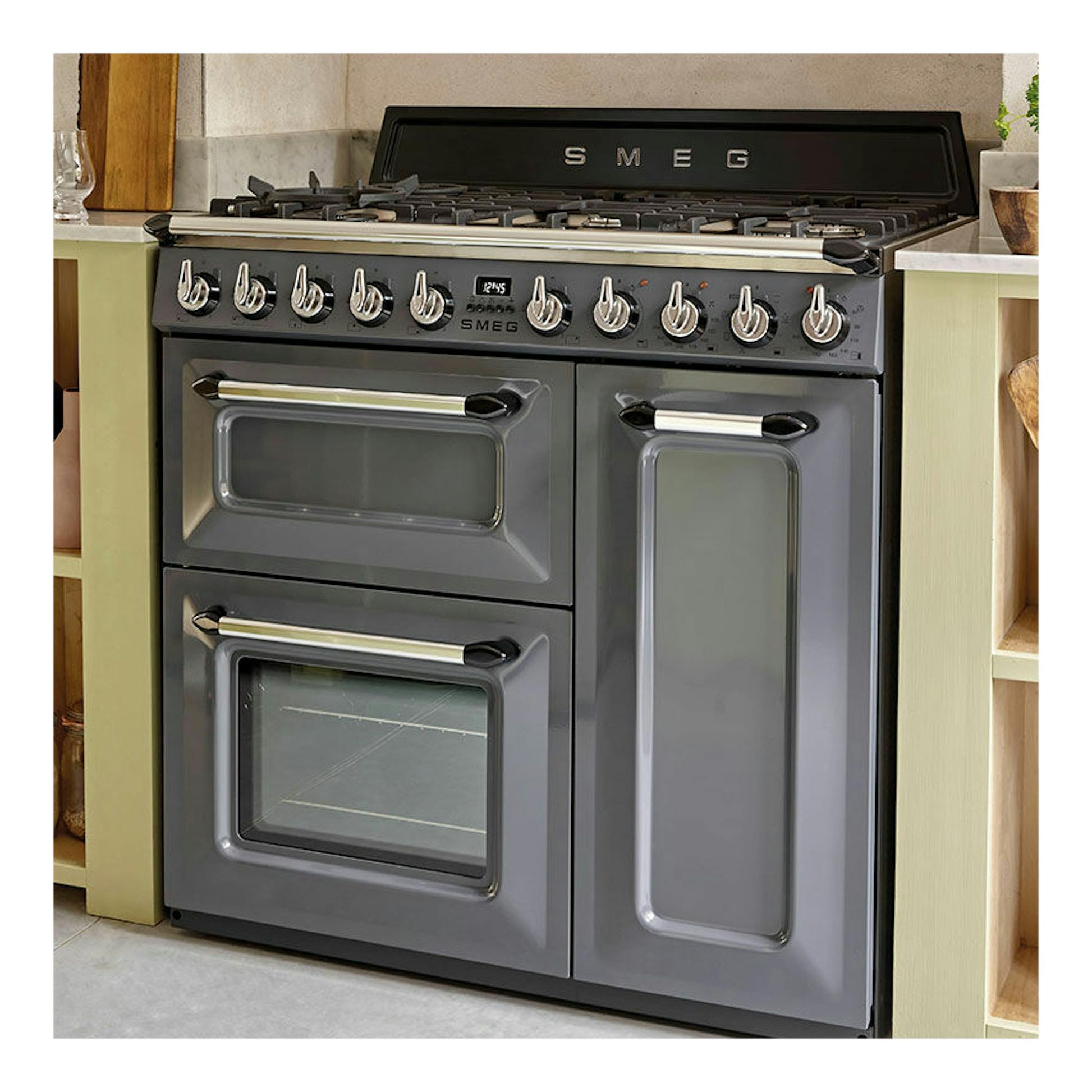 Cocina Smeg TR103GR gris, vista frontal, con placa de gas y tres puertas de horno.