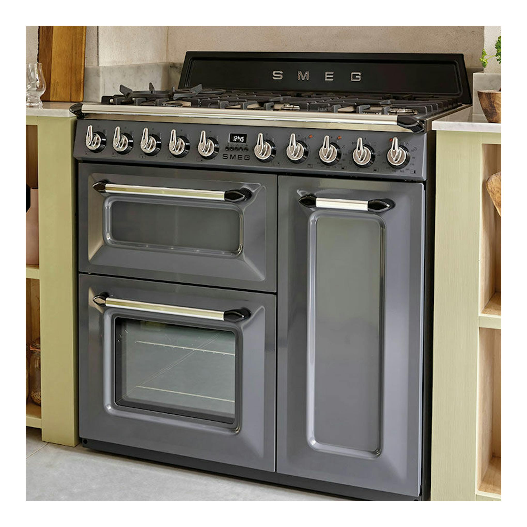 Cocina Smeg TR103GR gris, vista frontal, con placa de gas y tres puertas de horno.