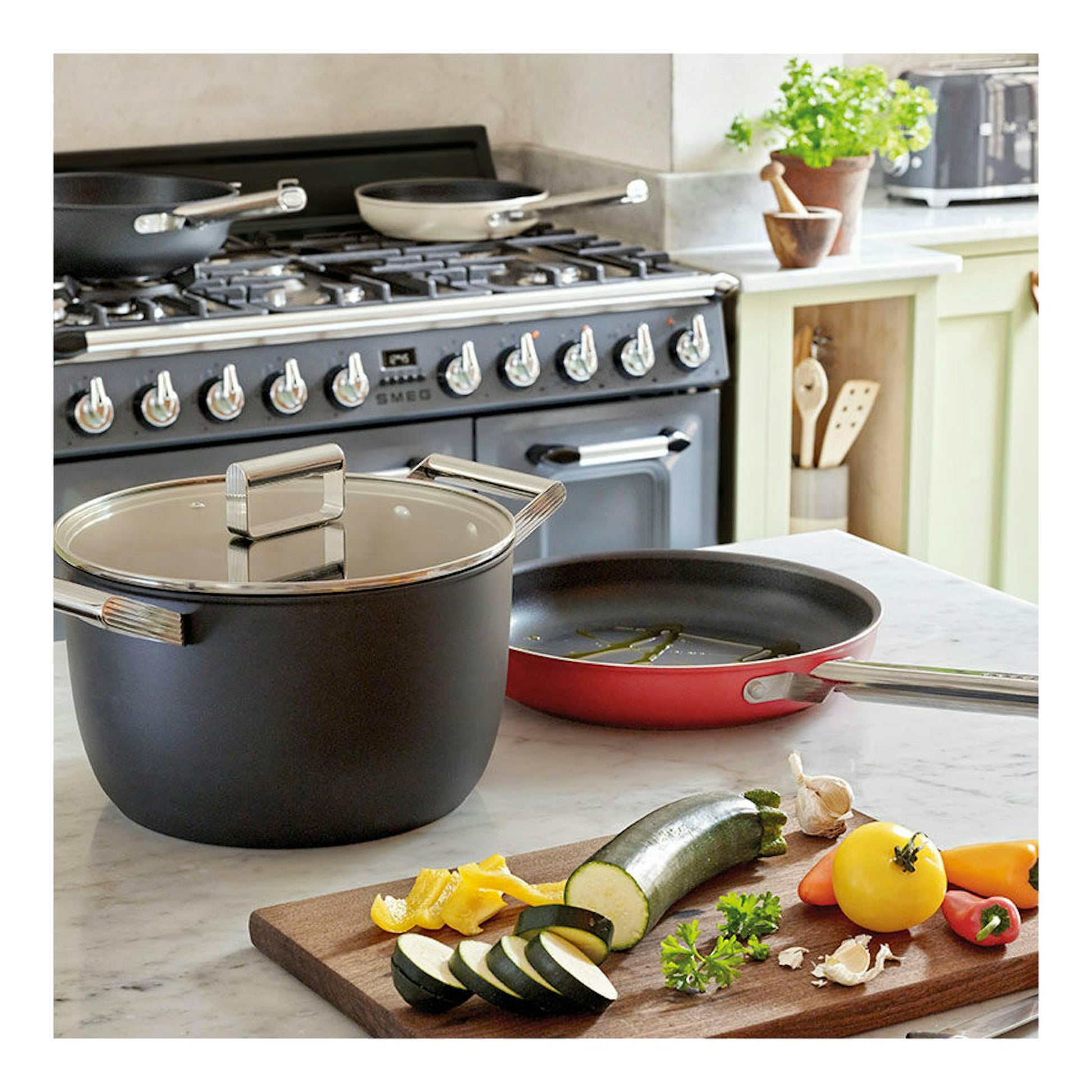 Cocina Smeg TR103GR gris, vista frontal, con ollas y sartén sobre la encimera en una cocina.