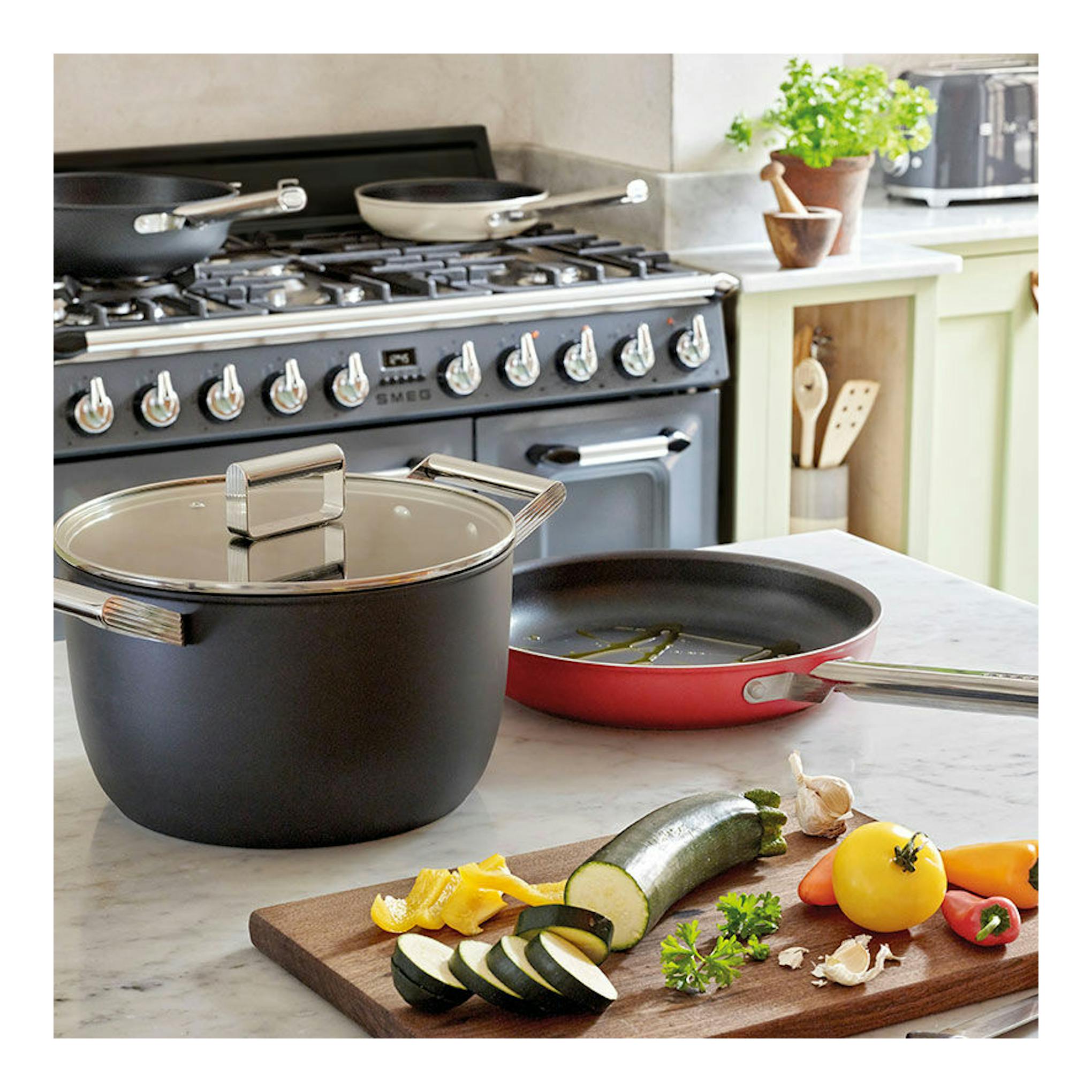 Cocina Smeg TR103GR gris, vista frontal, con ollas y sartén sobre la encimera en una cocina.