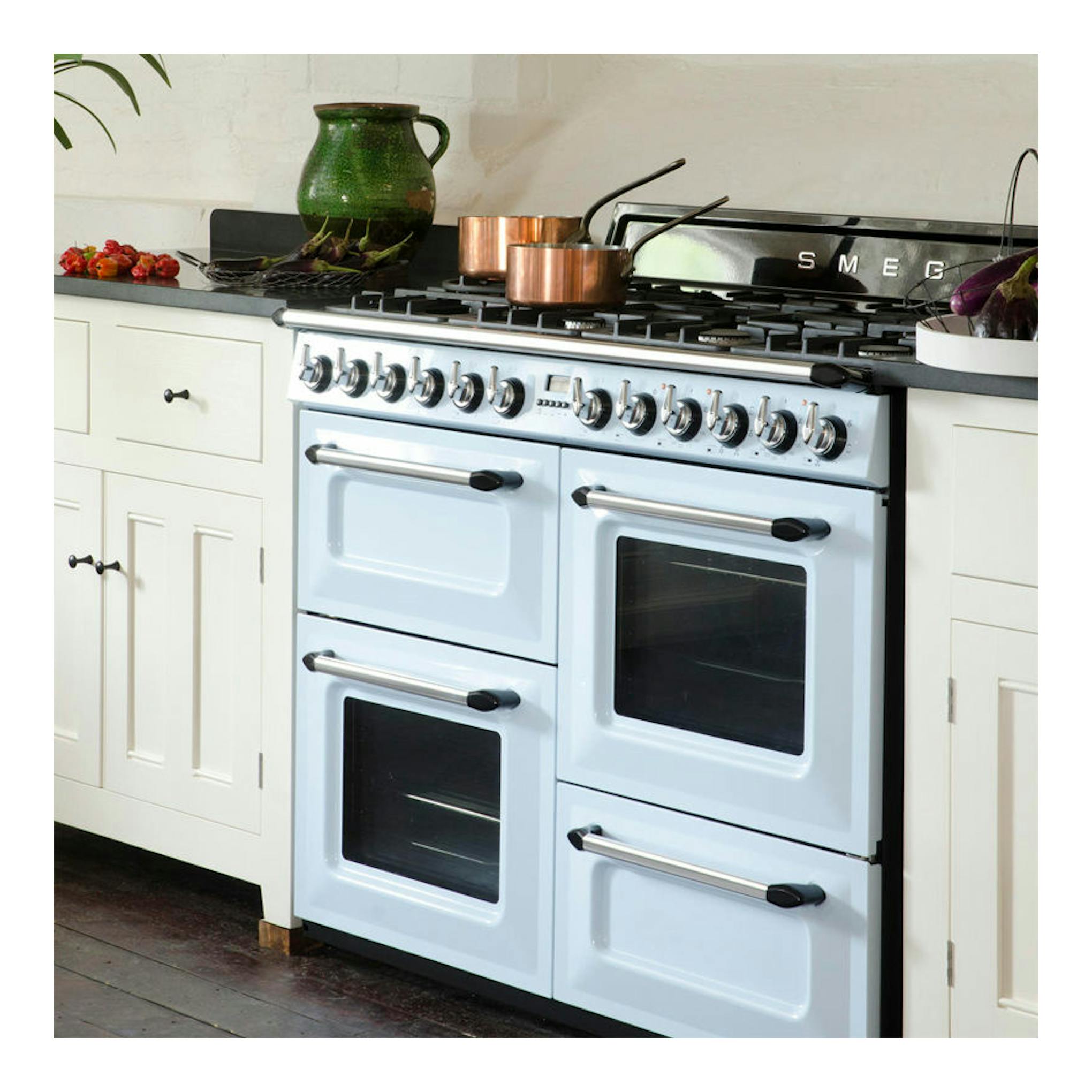 Cocina Smeg TR4110AZ azul claro, vista frontal, con cuatro hornos y encimera de gas.