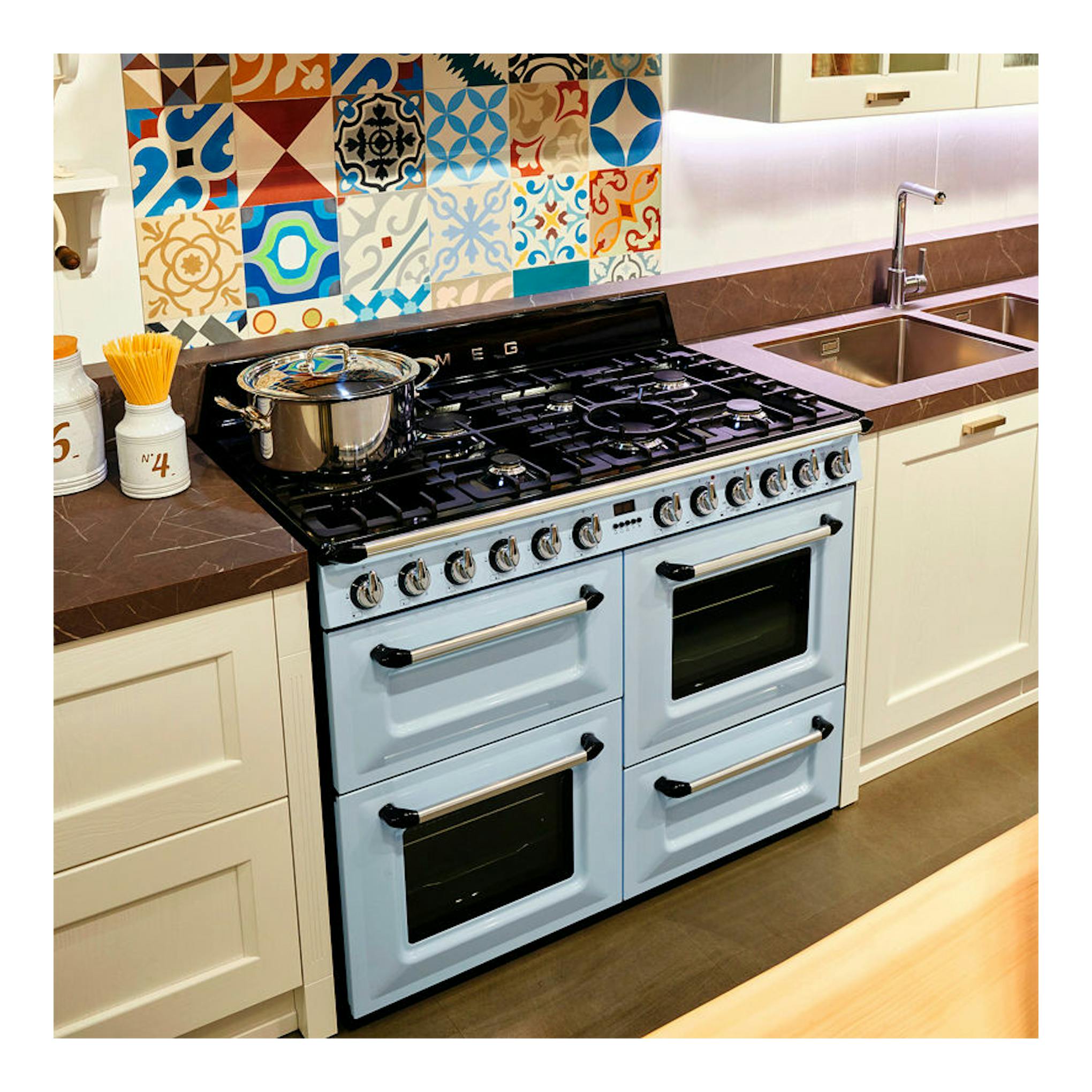 Cocina Smeg TR4110AZ azul claro, vista frontal en cocina, con placa negra, doble horno y mandos metálicos.