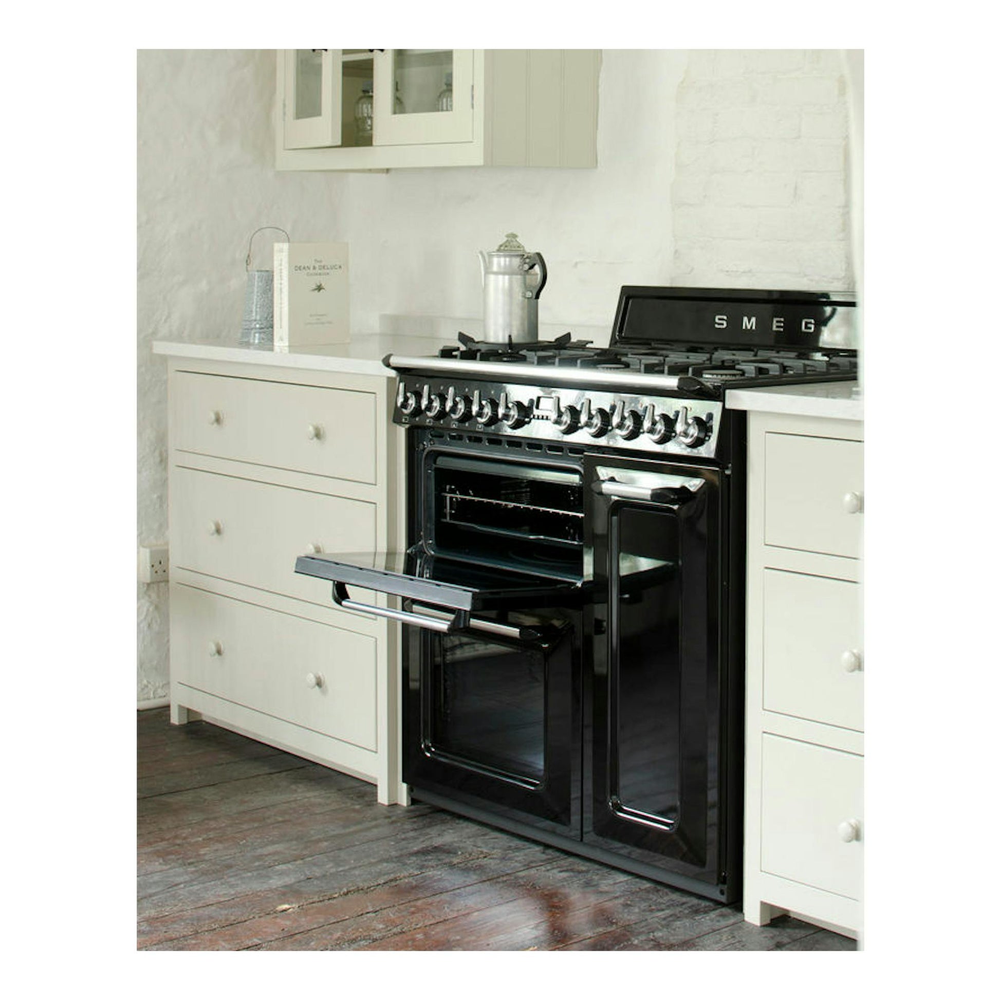 Cocina Smeg TR93BL negra, vista frontal, con horno abierto entre muebles blancos.