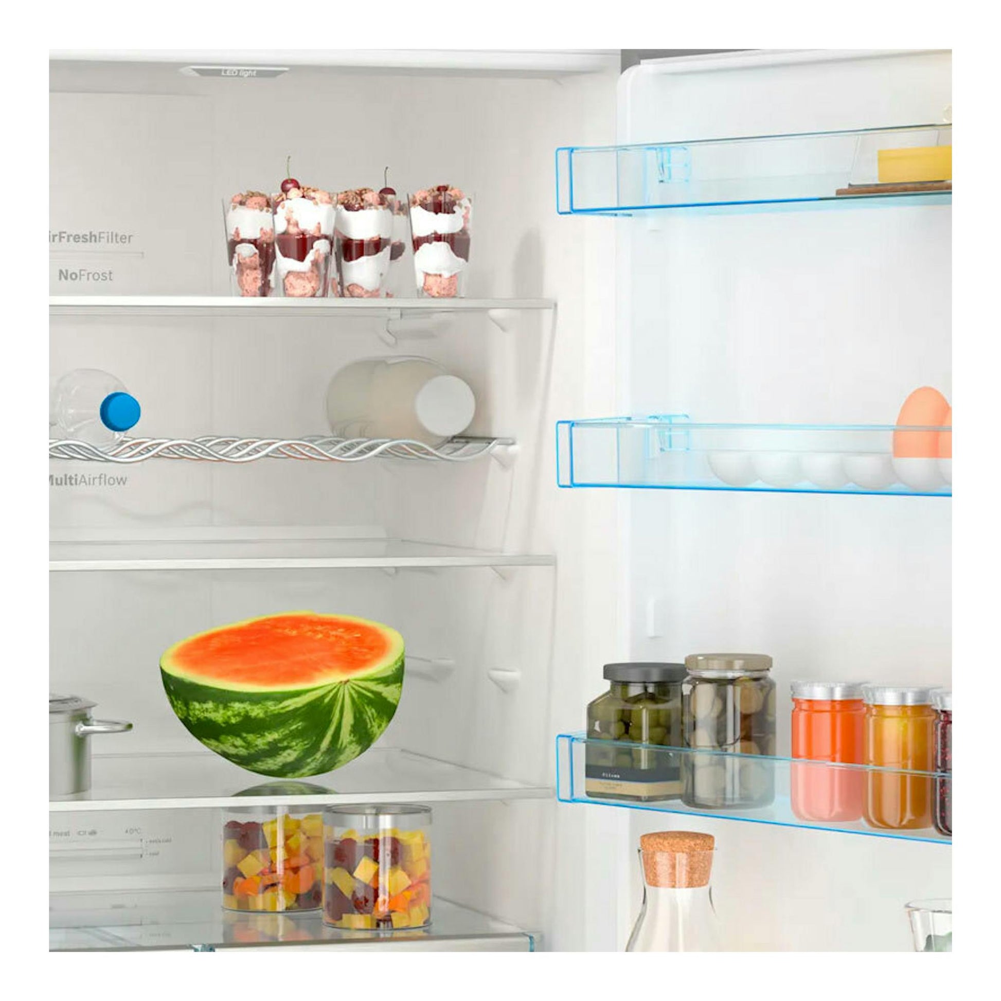 Bosch KGN56XIDR, interior de frigorífico combi abierto, con estantes de vidrio, sandía, tarros y vasos de postre.