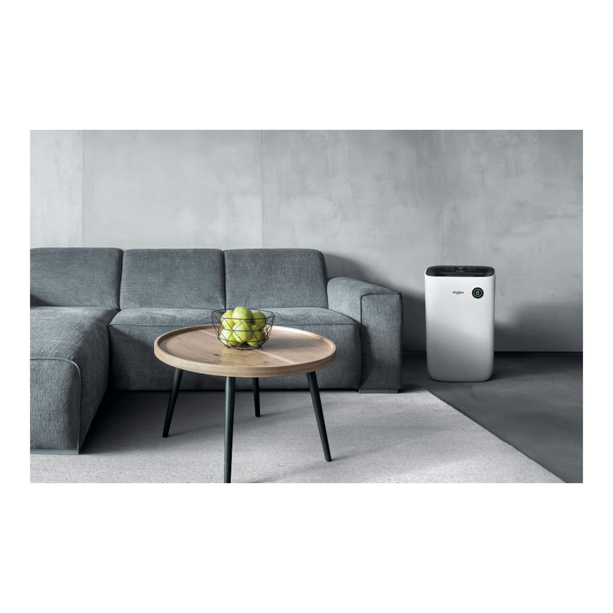 Deshumidificador Whirlpool DE20W5252 blanco, en un salón junto a sofá gris y mesa redonda con un bol de manzanas.