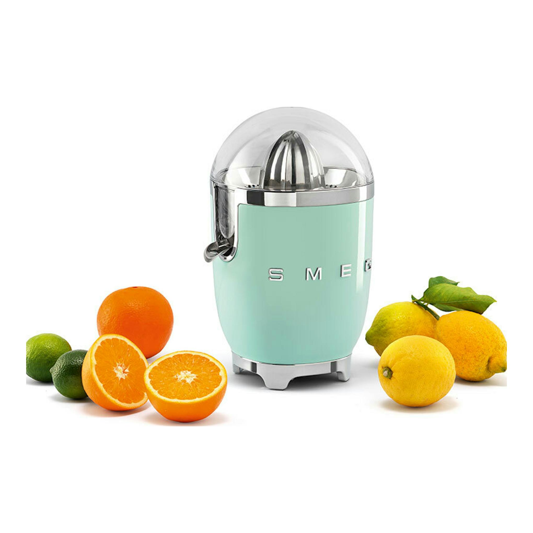 Exprimidor Smeg CJF11PGEU verde menta, vista frontal, junto a naranjas, limas y limones.