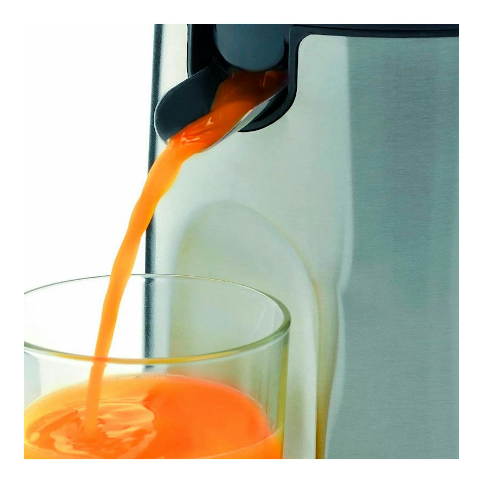 Exprimidor WMF Stelio de acero inoxidable vertiendo zumo de naranja en un vaso, vista en primer plano.