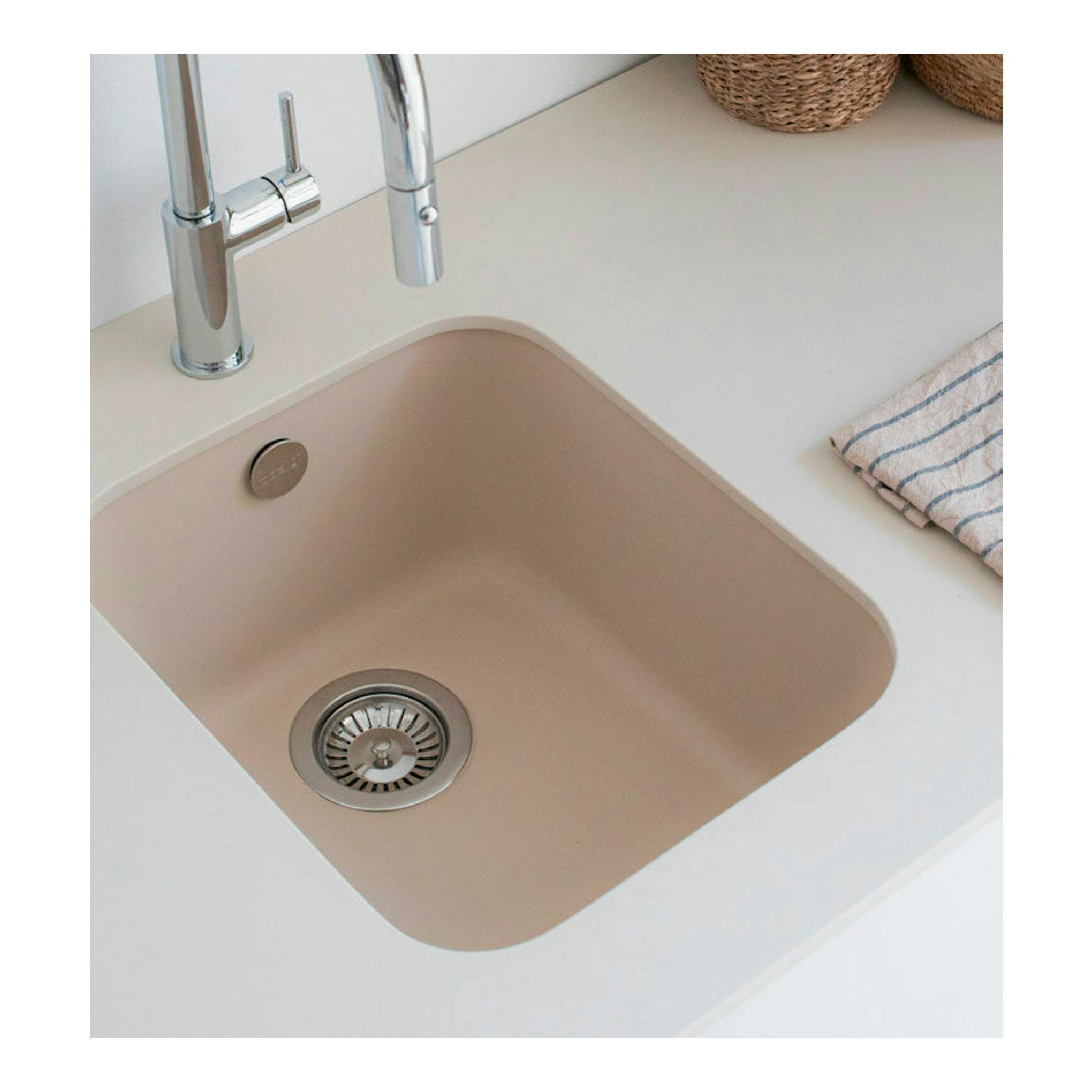 Fregadero Poalgi Gandia 35 beige, vista superior inclinada, empotrado en encimera blanca con grifo cromado.