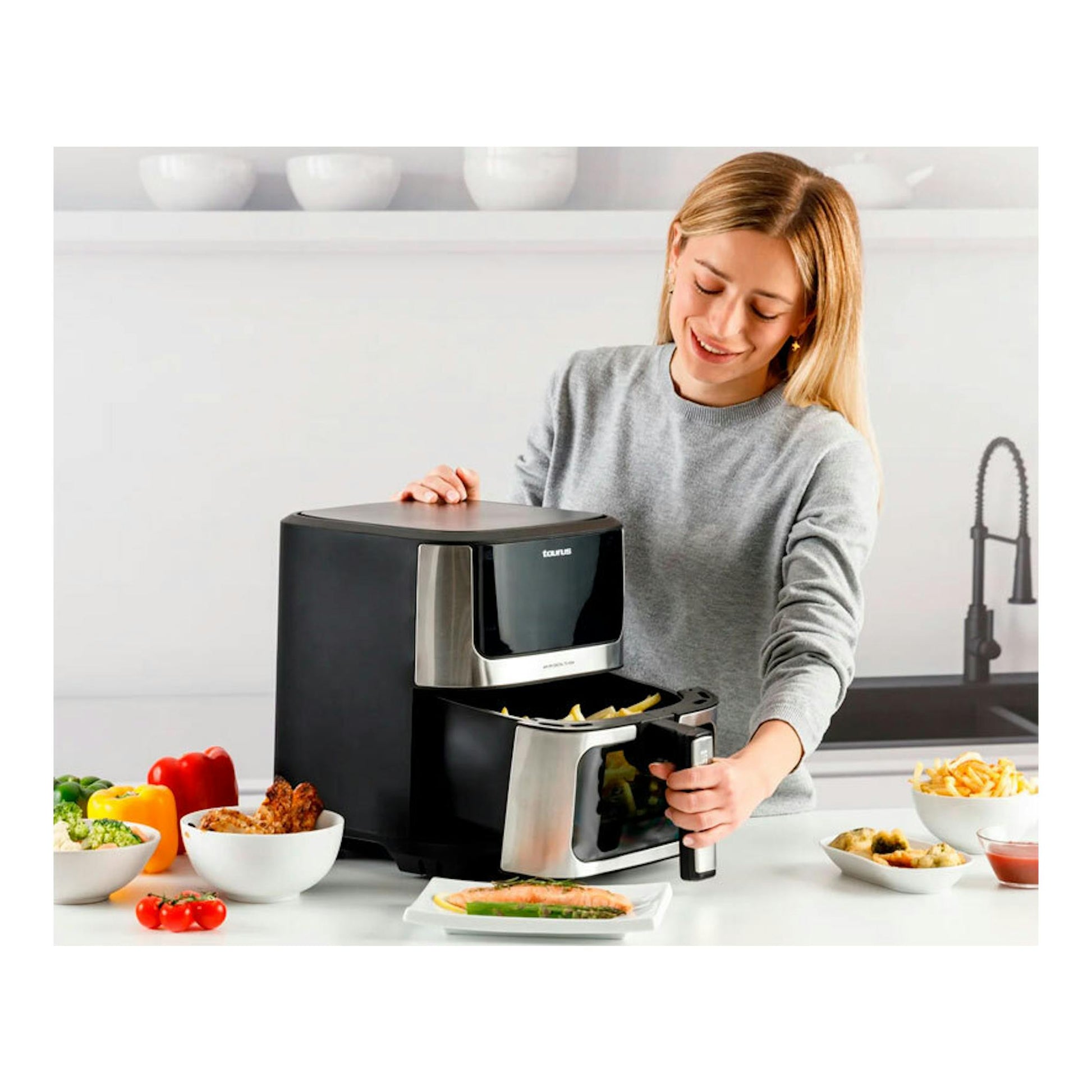 Freidora de aire Taurus Digital 7 negra, vista frontal en cocina, con cajón abierto y una mujer usándola.