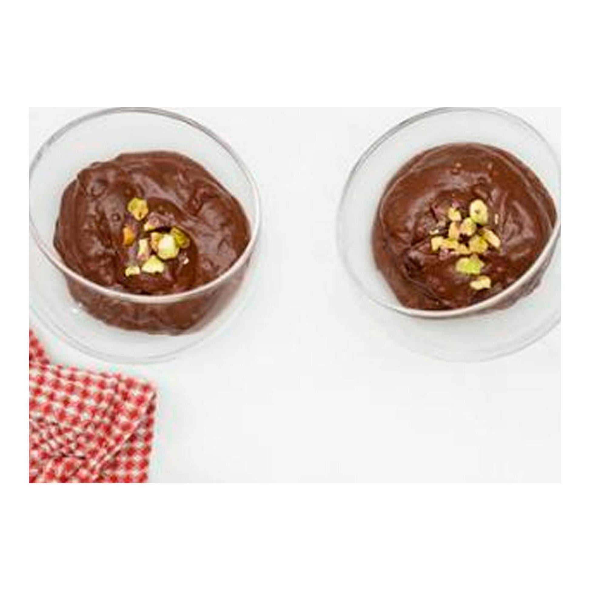Vista superior de dos cuencos de vidrio con mousse de chocolate y trozos de pistacho sobre fondo blanco.