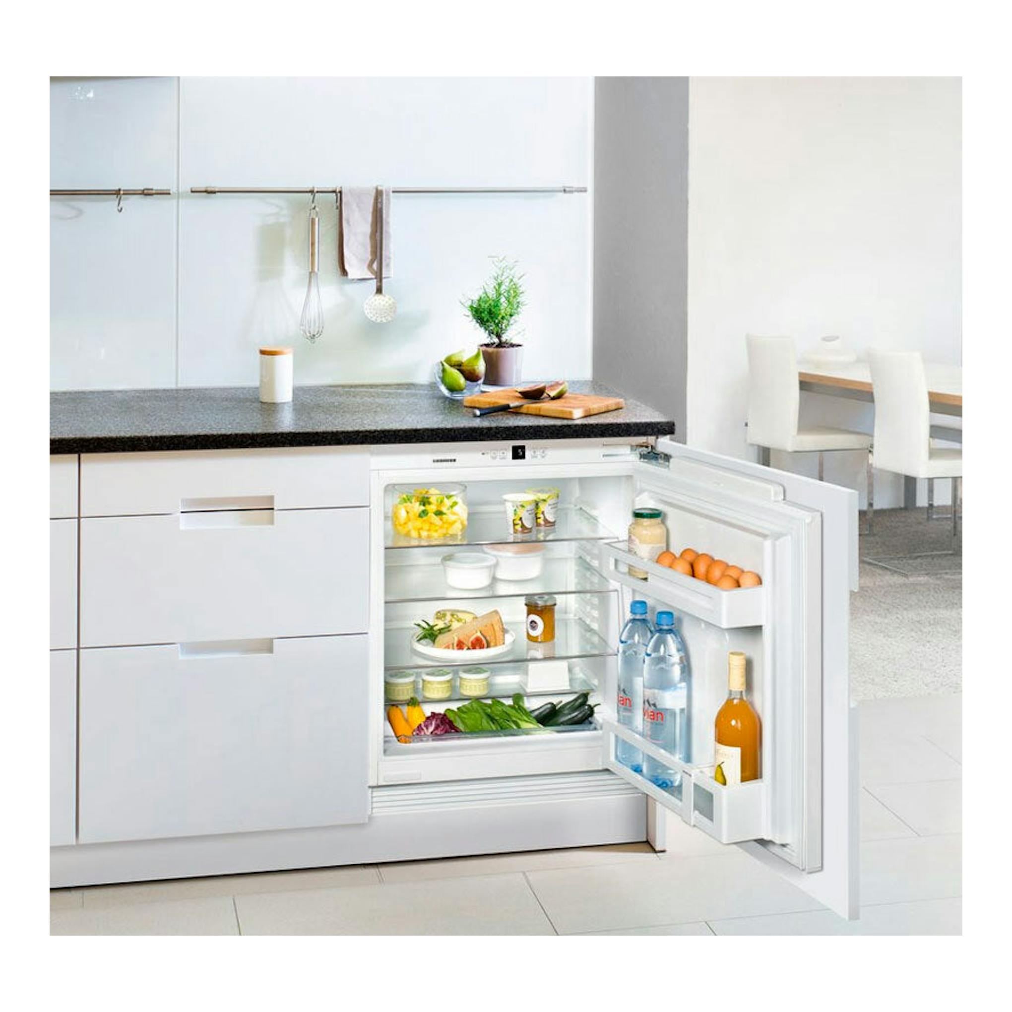 Frigorífico integrable Liebherr UIK 1510 abierto de frente en cocina blanca, con estantes y alimentos.