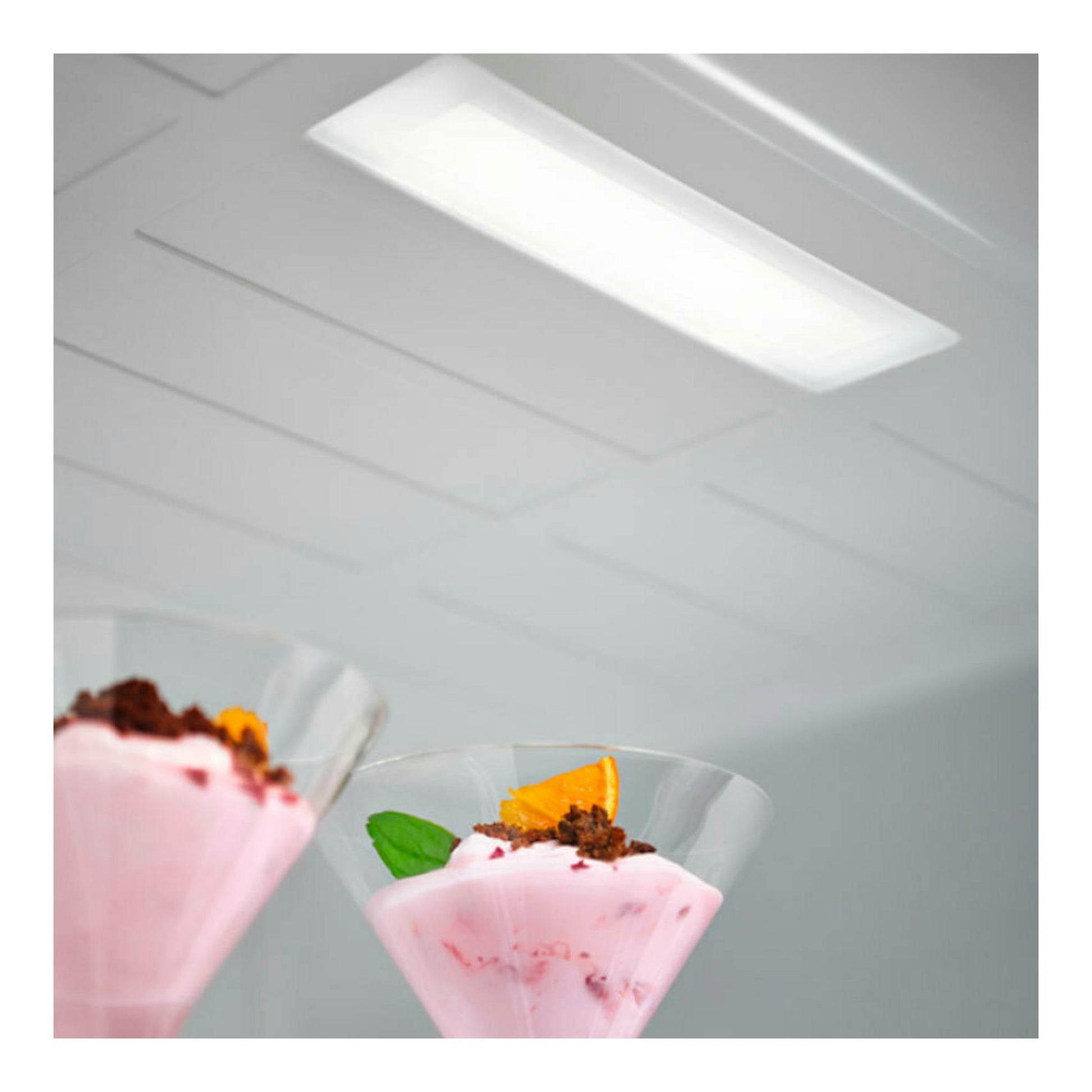 Interior de frigorífico con luz LED superior y dos copas de postre rosa, vista en ángulo.