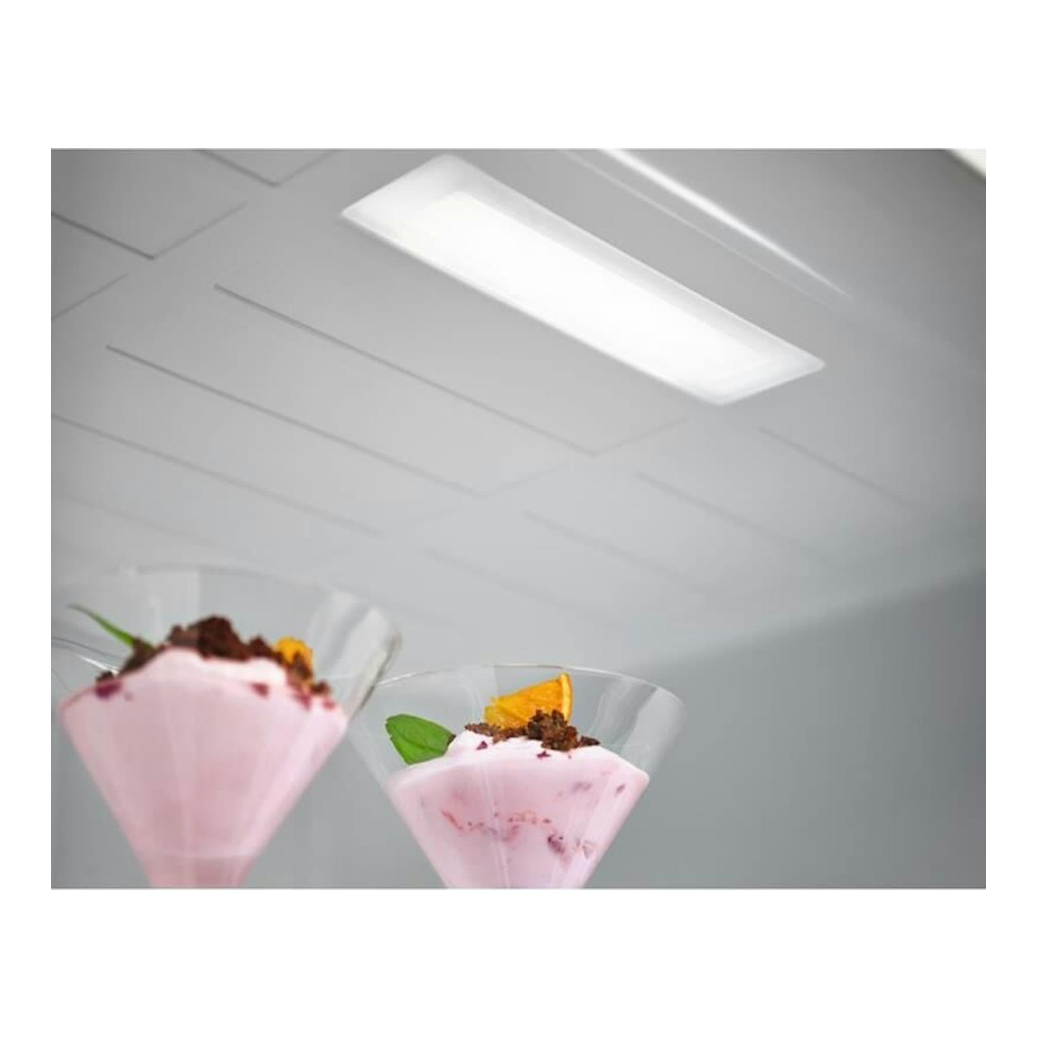 Interior de frigorífico combi AEG RCB736D3MW blanco, vista en ángulo, con luz superior y copas con postre.