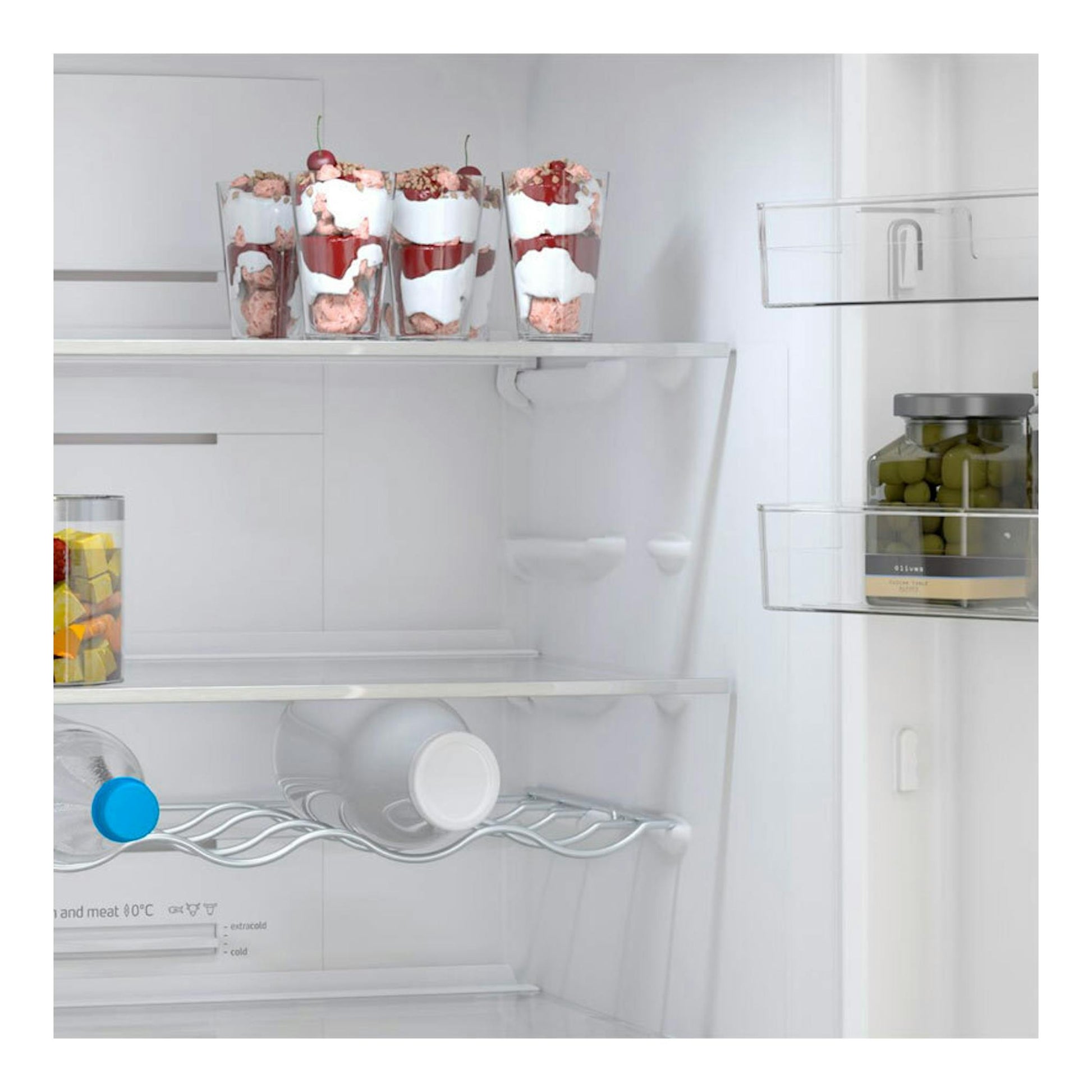 Interior de frigorífico blanco en vista frontal, con copas de postre, botellas y tarro de aceitunas.