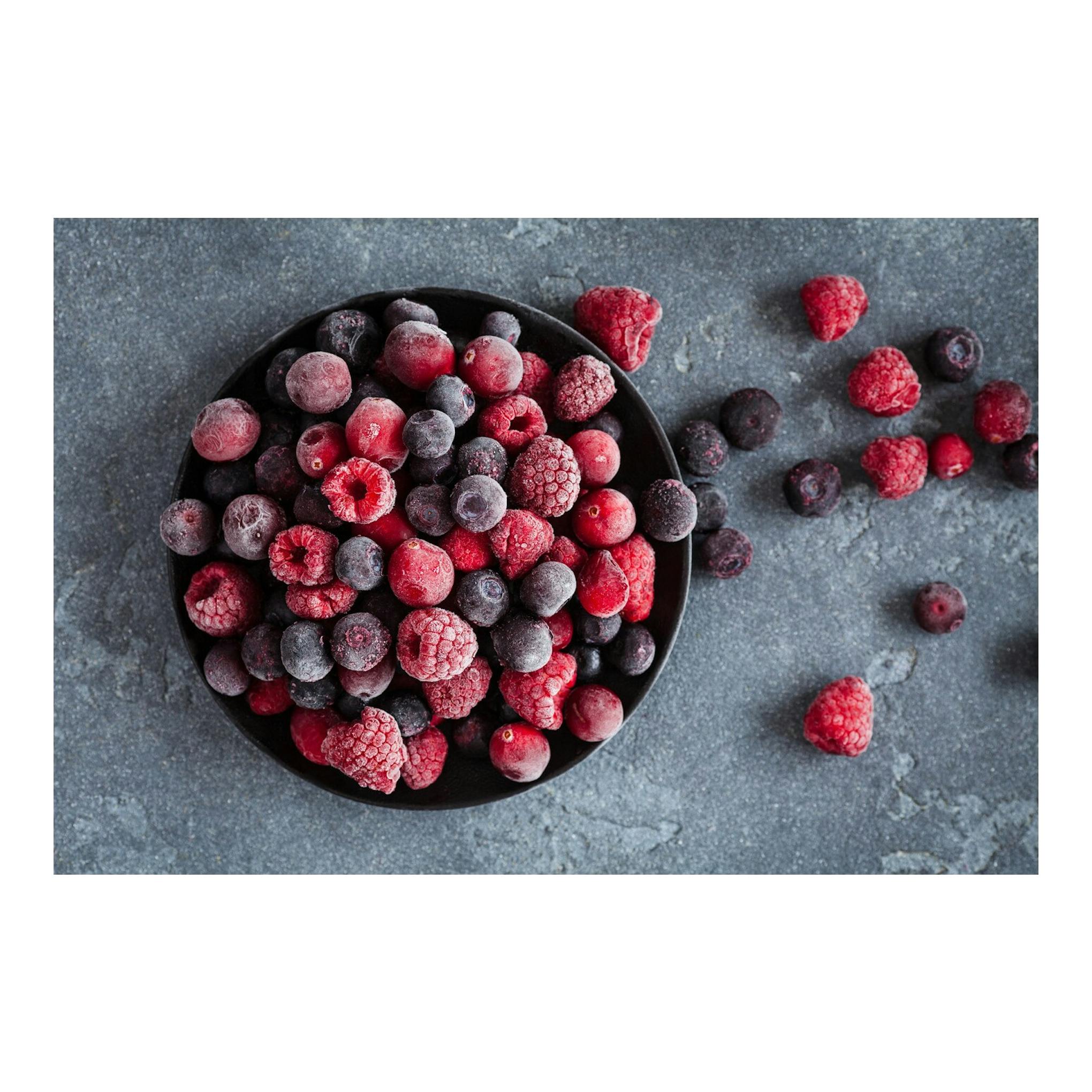 Vista cenital de un cuenco negro con frutos rojos y morados congelados sobre fondo gris.