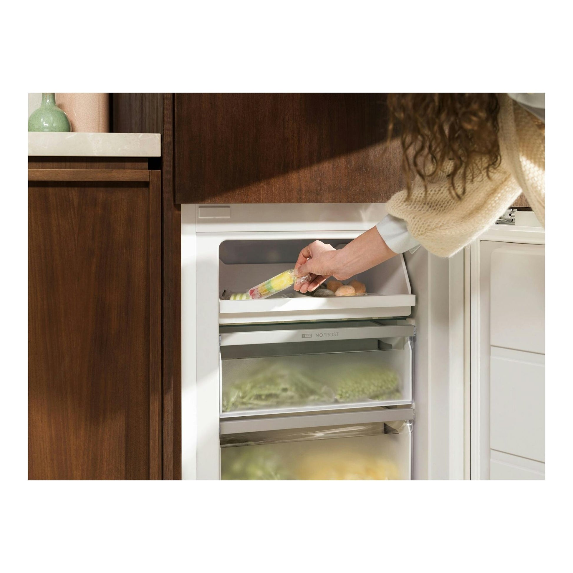 Frigorífico combi integrable Electrolux LNA6LE18S, vista frontal, blanco, con cajones abiertos y una mano colocando un helado.