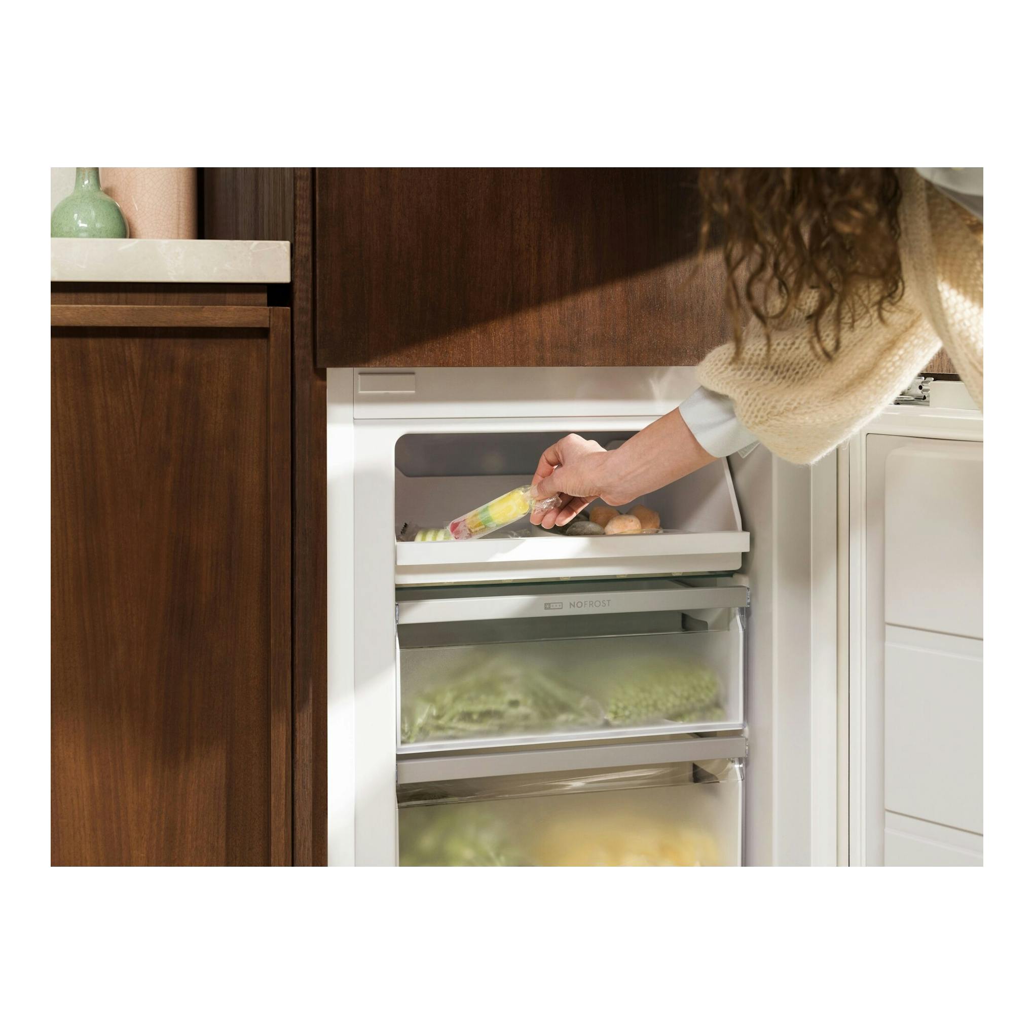 Frigorífico combi integrable Electrolux LNA6LE18S, vista frontal, blanco, con cajones abiertos y una mano colocando un helado.
