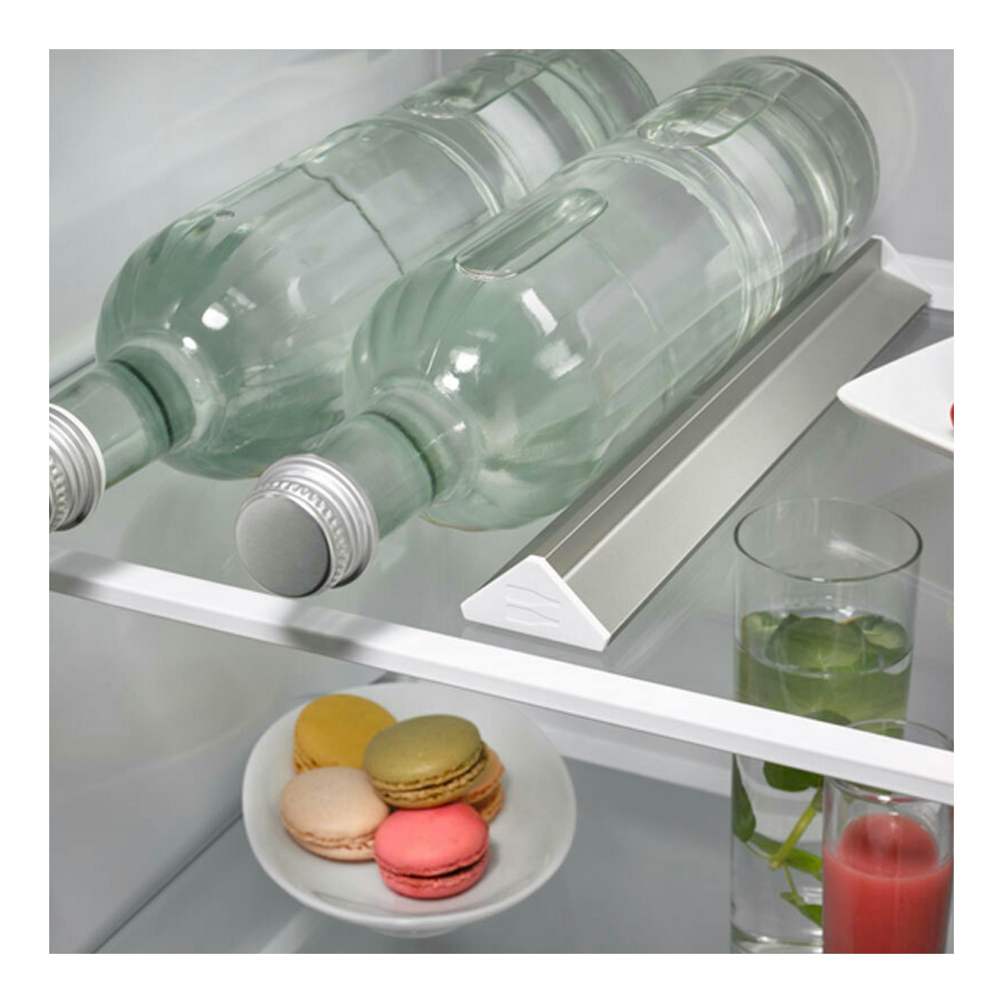 Interior de frigorífico combi integrable AEG OSC7G181ES, con botellas, vasos y macarons en estantes de vidrio.