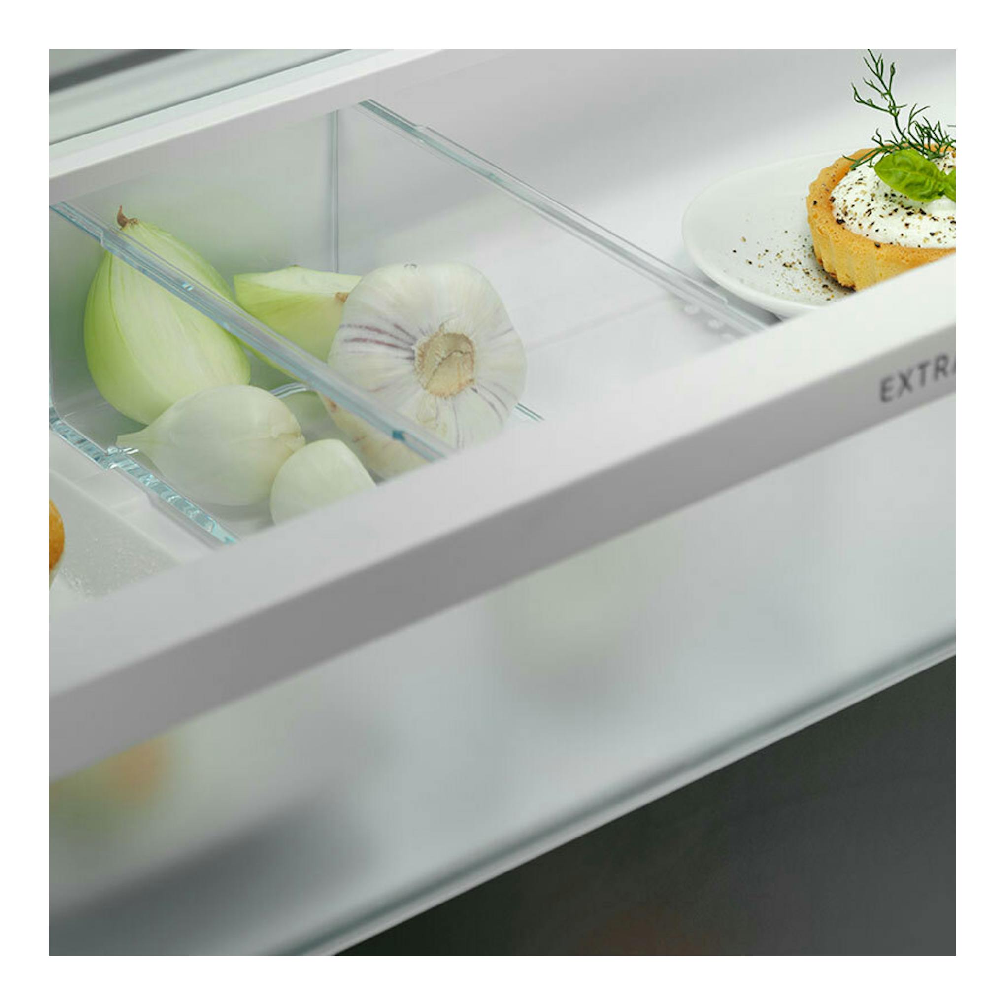 Interior de frigorífico integrable Electrolux ENG7TE75S, en ángulo, con cajón transparente y alimentos.