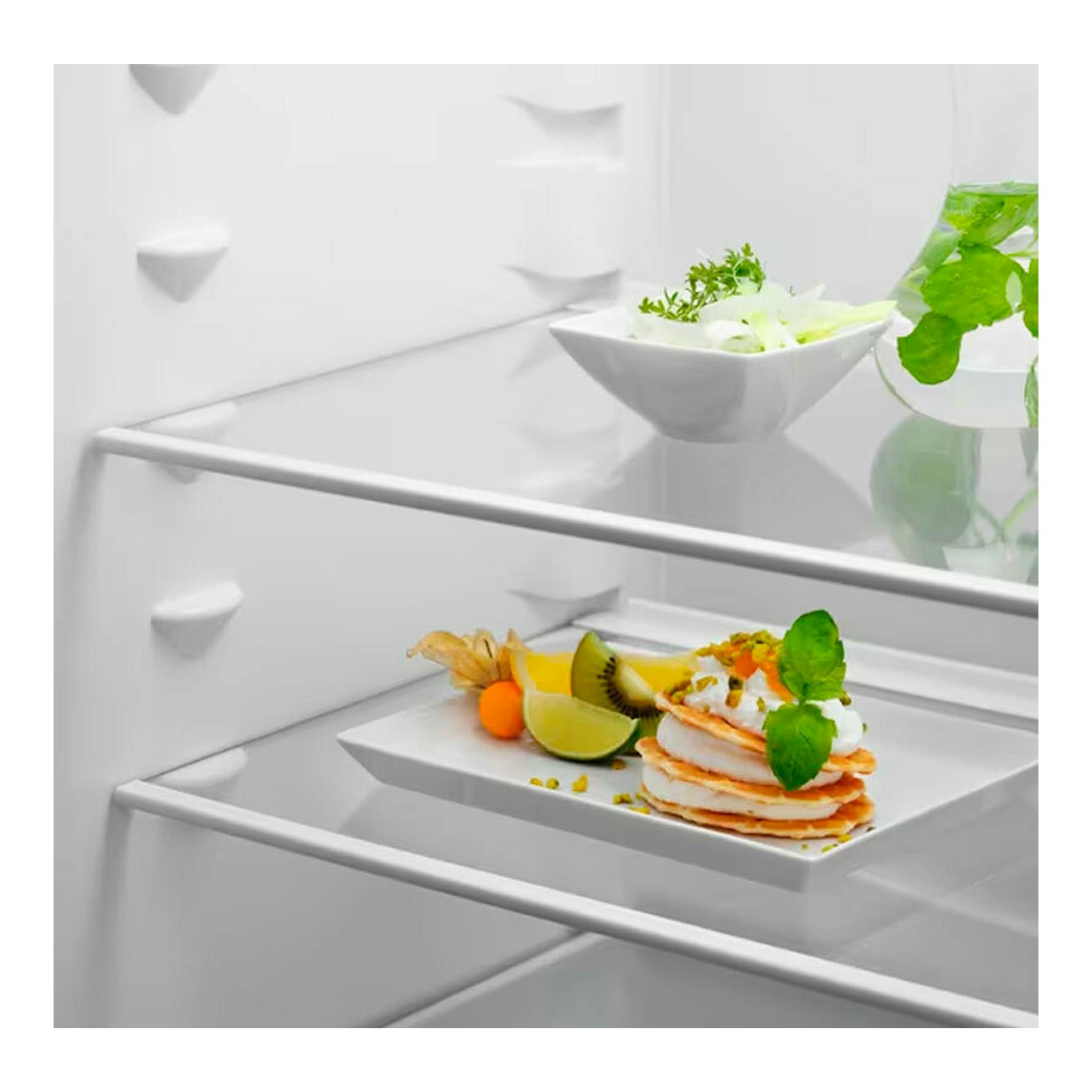 Interior de frigorífico combi integrable Electrolux LNS5LE18S, vista frontal, con estantes blancos y platos de comida.