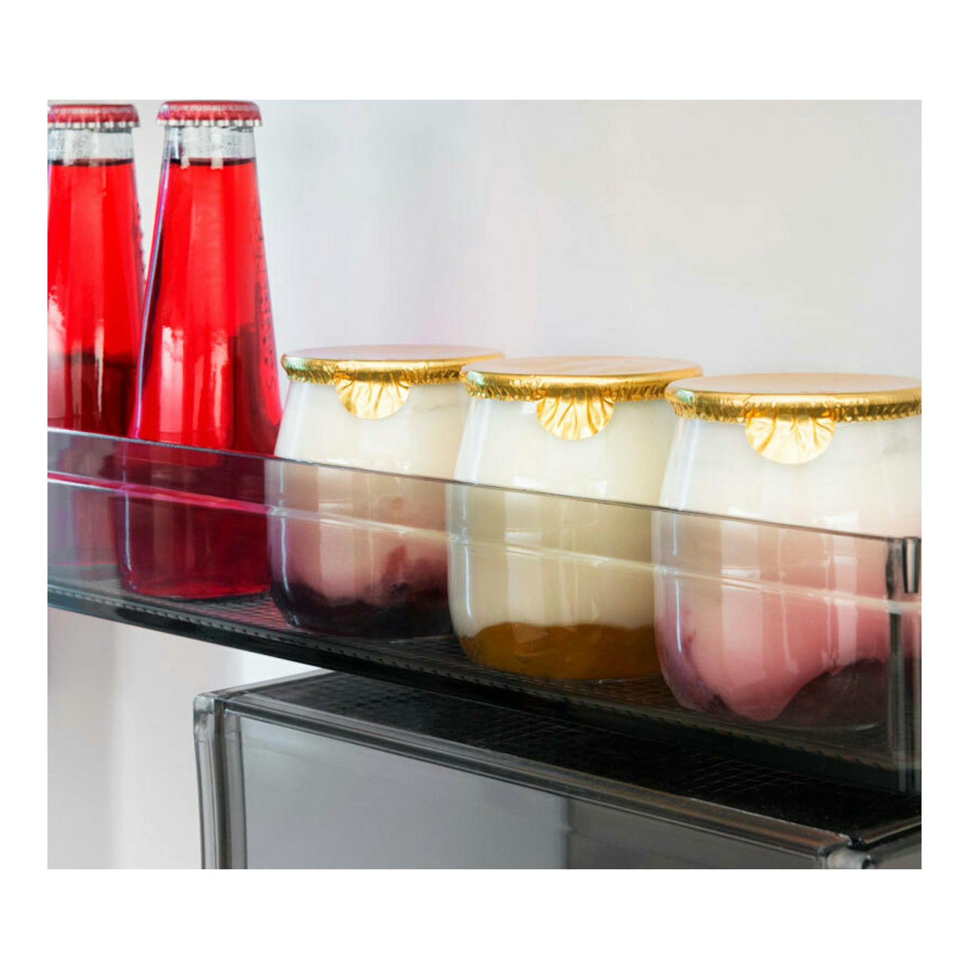 Interior de un frigorífico integrable: estante de la puerta con botellas rojas y tarros de vidrio con tapa dorada.