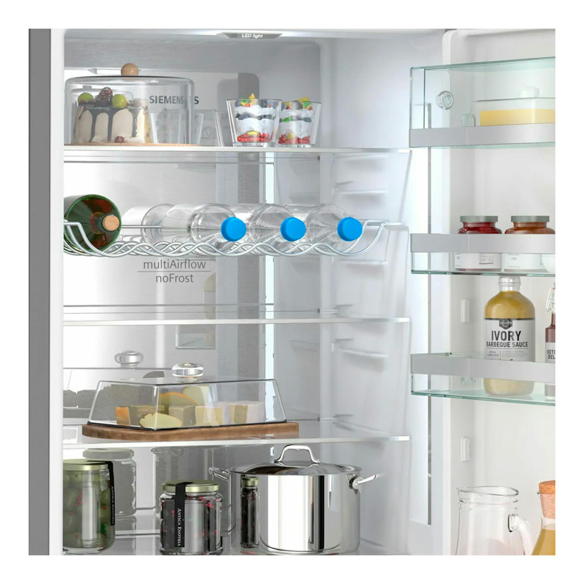 Interior de frigorífico Siemens KG39NSBBF, vista frontal, con estantes de cristal, botellas, tarros y recipiente metálico.