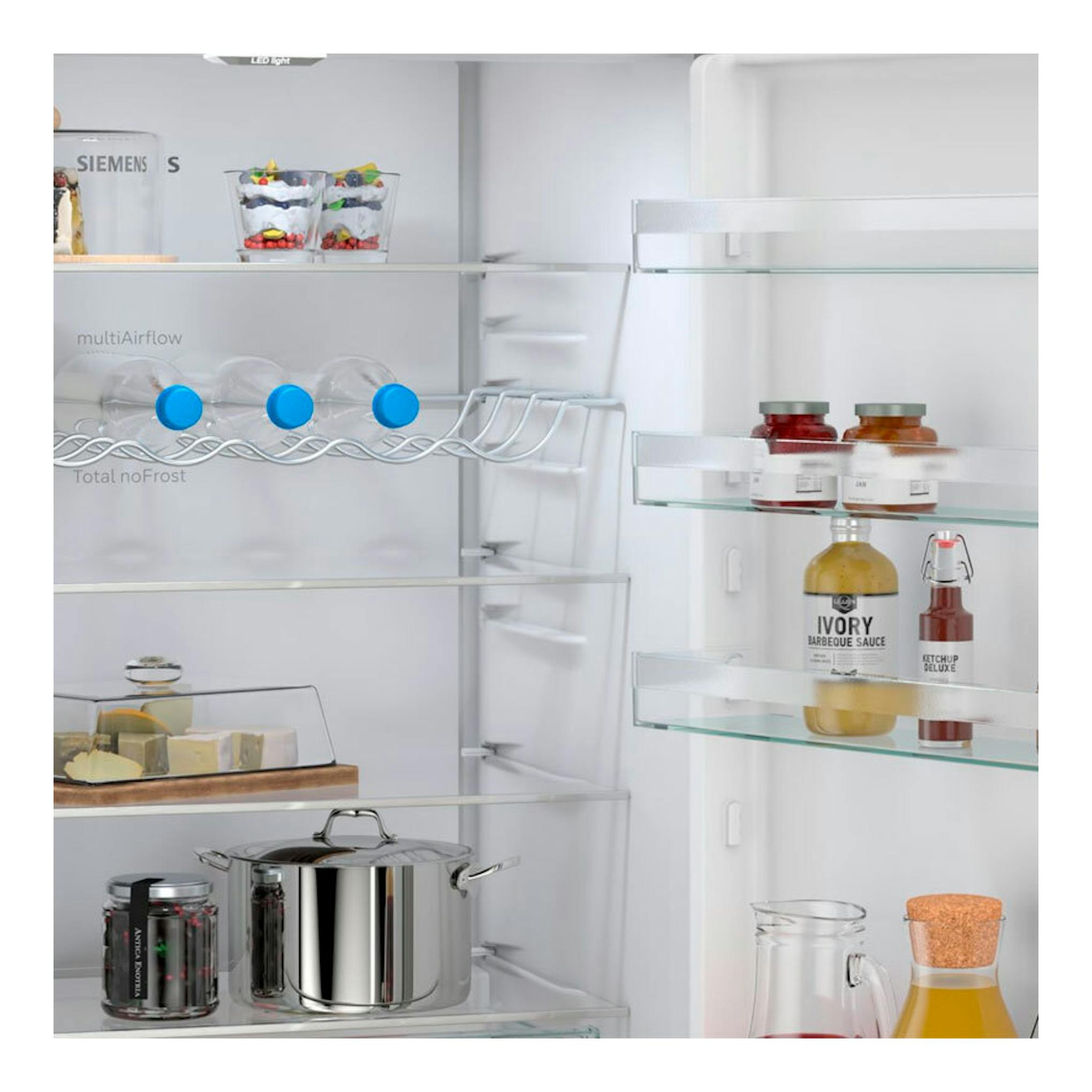 Vista frontal del interior de un frigorífico combi Siemens KG49NXIDF inox, con estantes de cristal y alimentos.