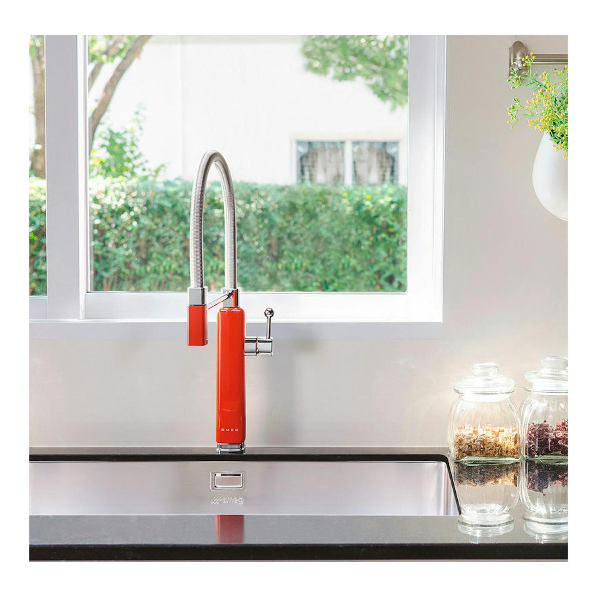 Grifo de cocina Smeg MDF50RD rojo, vista frontal, con caño flexible metálico sobre fregadero.