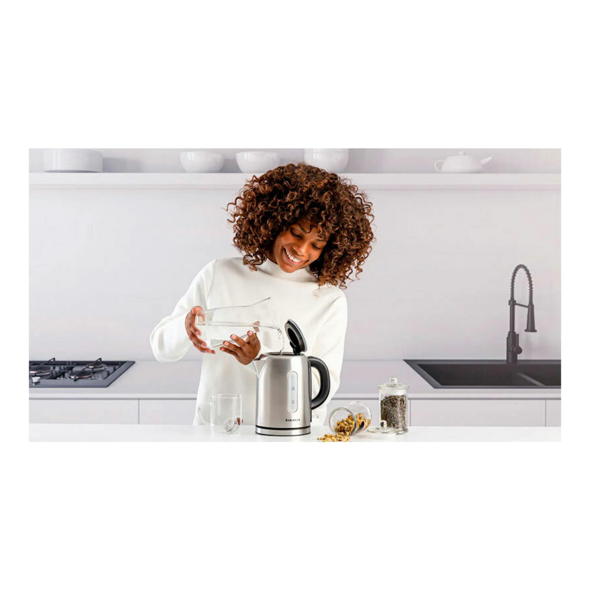 Hervidor eléctrico Taurus Selene Compact de acero inoxidable en cocina, con una mujer vertiendo agua.