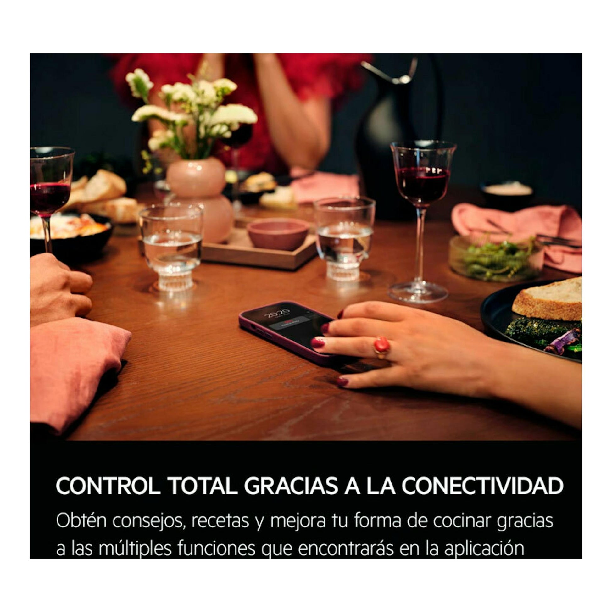 AEG GS6PB51FAB: mano usando un móvil sobre una mesa de cena con copas, platos y comida.
