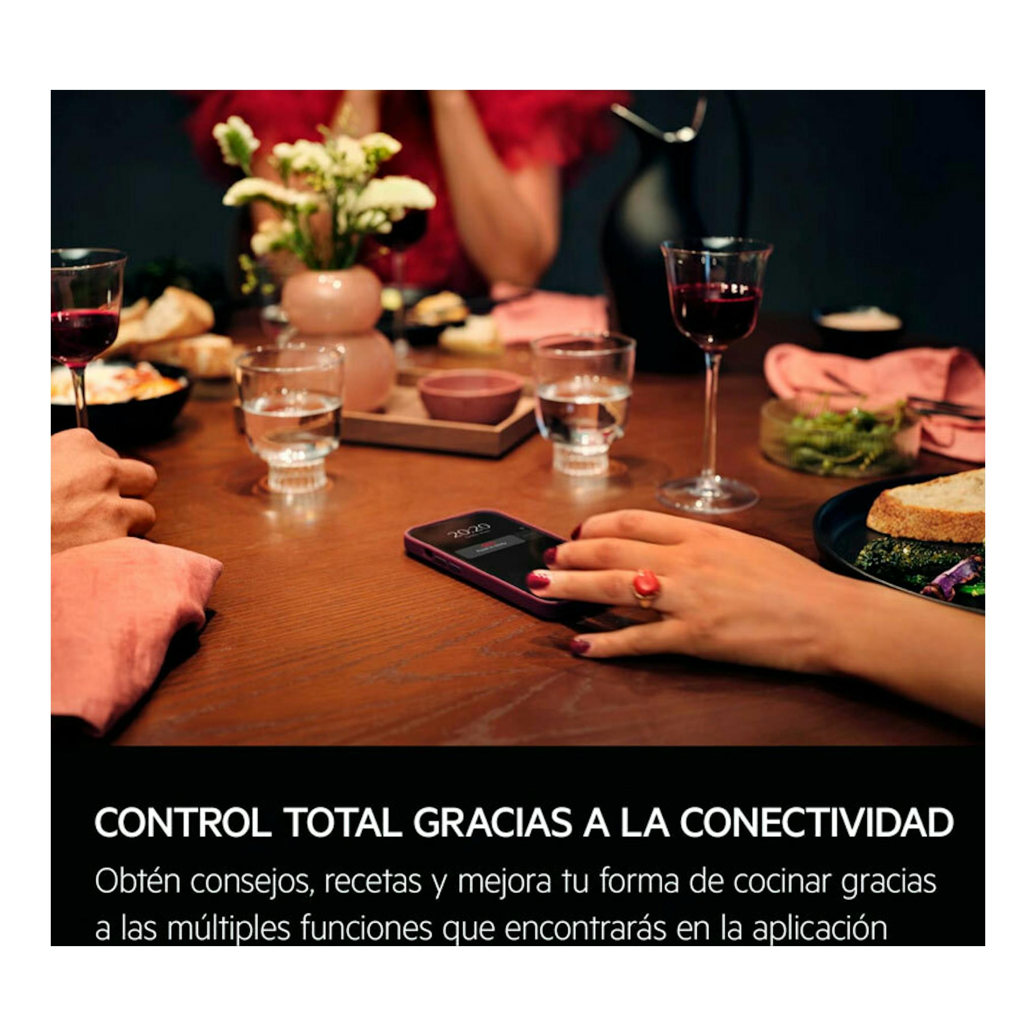 AEG GS6PB51FAB: mano usando un móvil sobre una mesa de cena con copas, platos y comida.