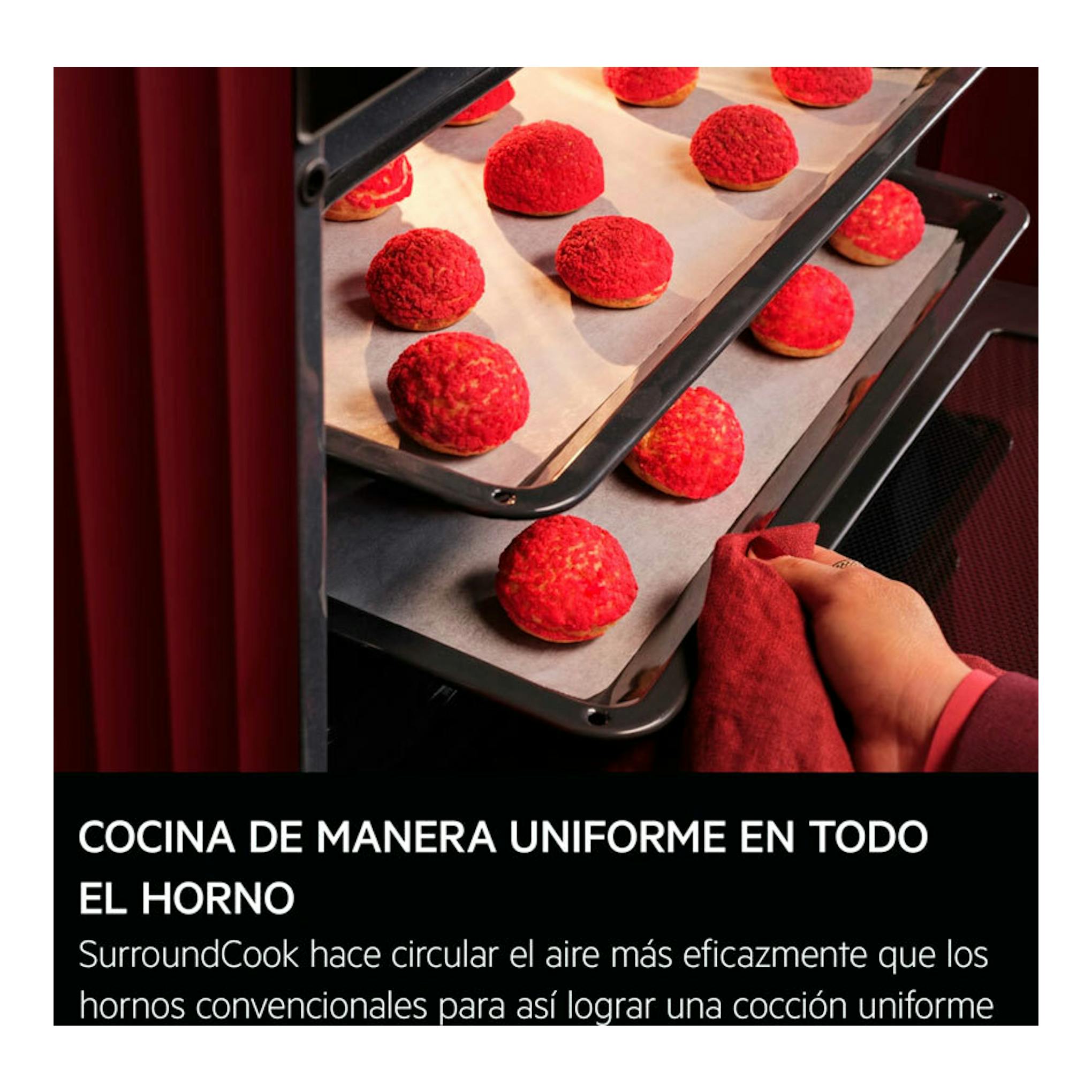 Vista frontal del horno AEG GU5PB43FSM inox, con bandejas y bollos rojos; una mano sostiene un paño.