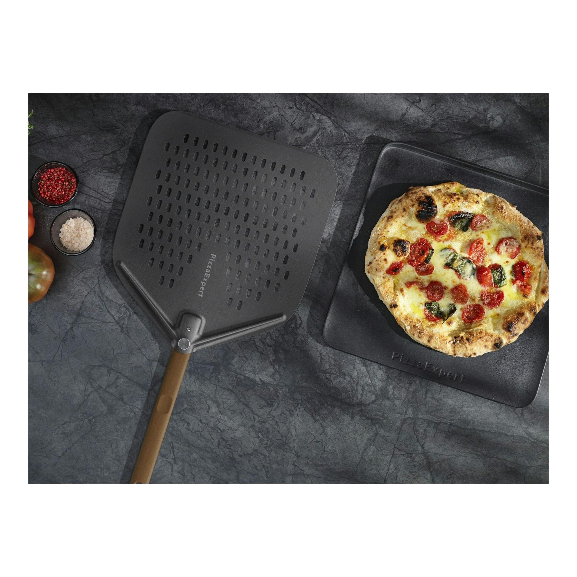 Vista cenital de pala PizzaExpert negra, bandeja con pizza y pequeños cuencos de ingredientes.