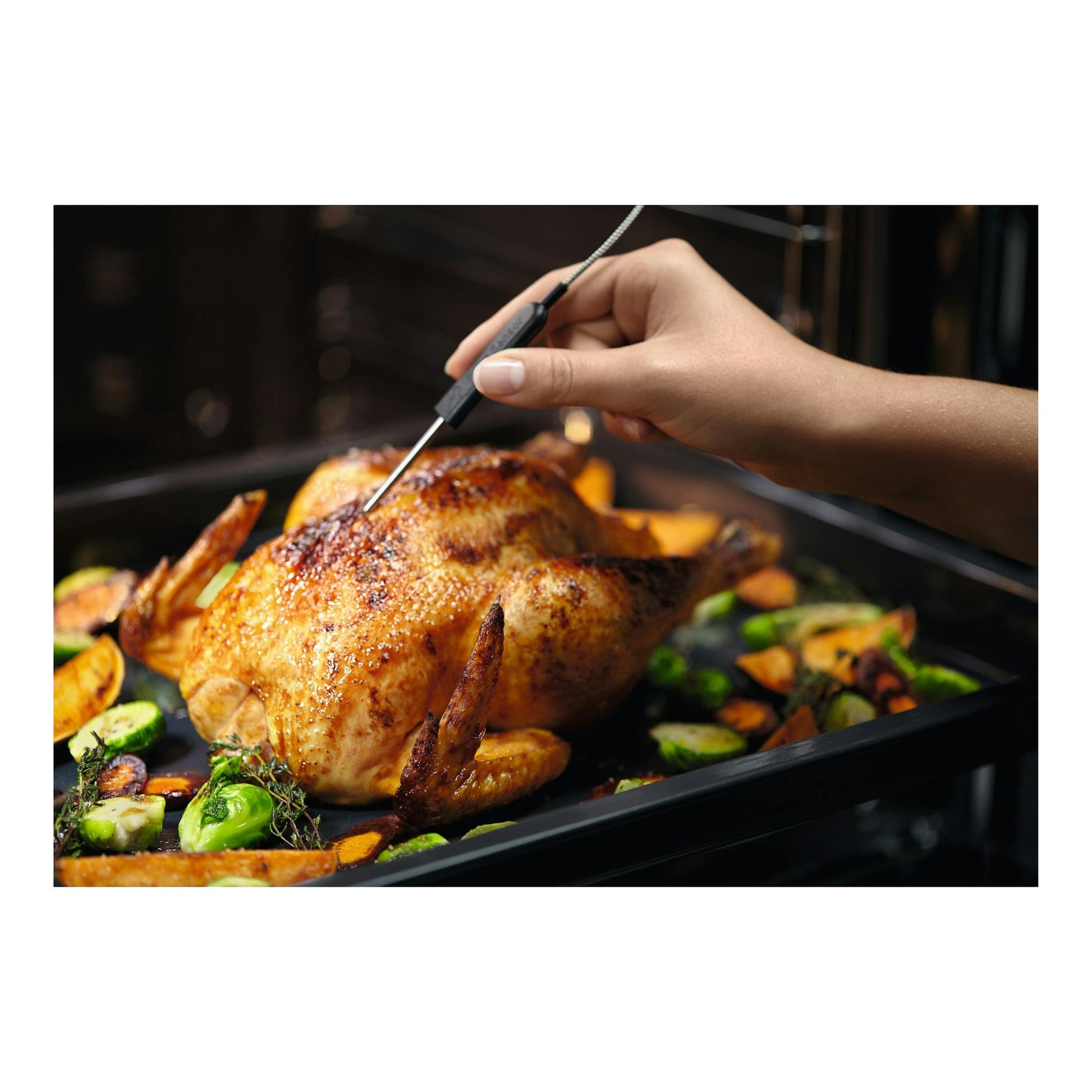 Horno Electrolux EOD6P77X negro, vista interior con pollo asado y una mano usando un termómetro.