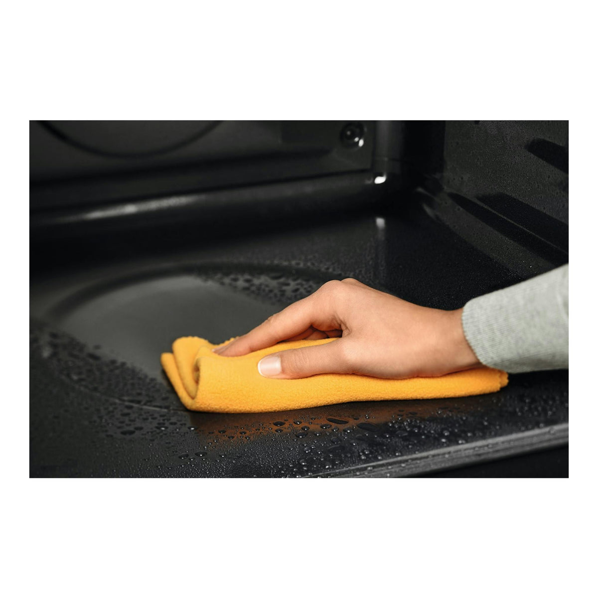 Interior de horno Electrolux EOF3H40BX negro, con una mano limpiando con un paño amarillo.