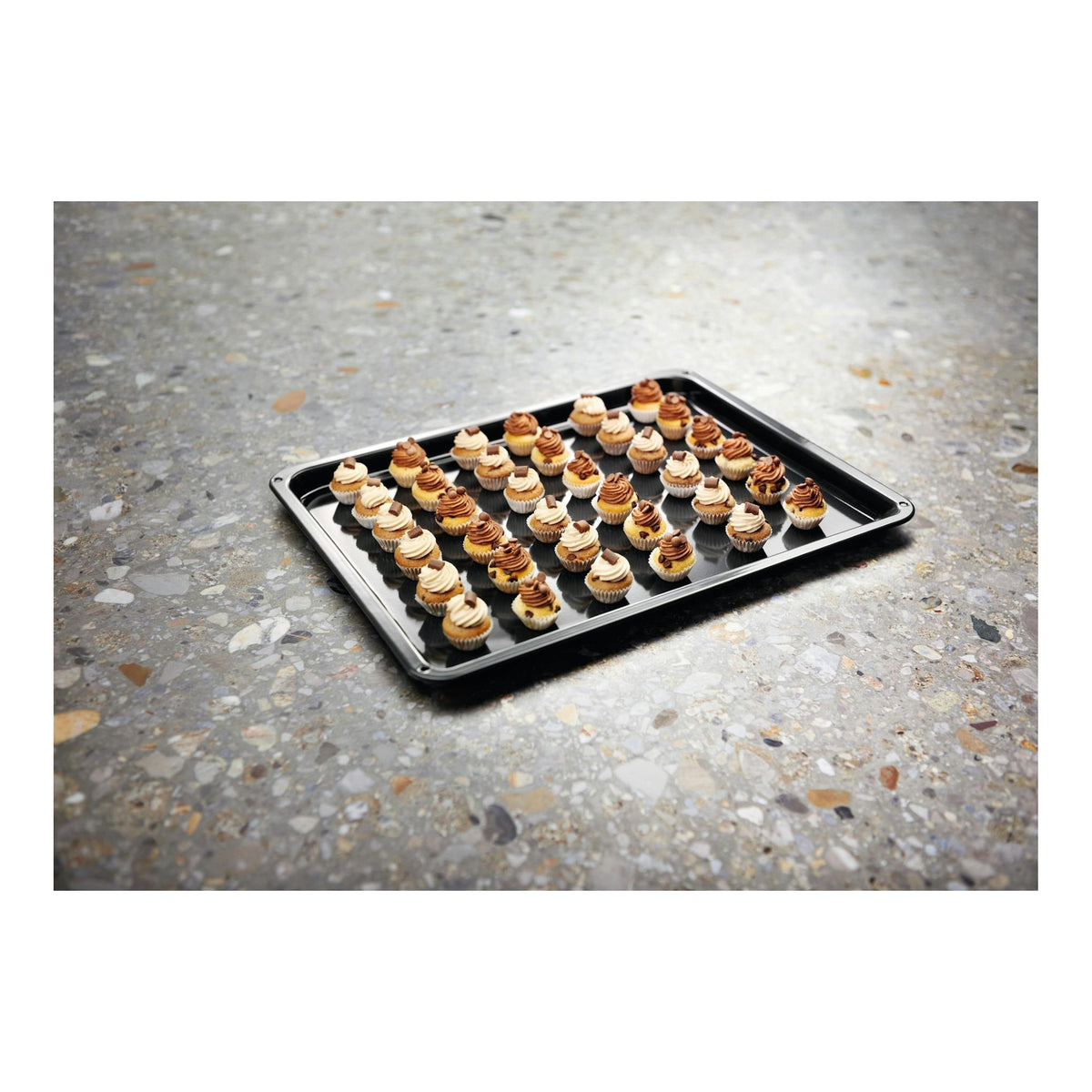 Bandeja de horno negra con mini cupcakes decorados, vista en ángulo sobre encimera de piedra.
