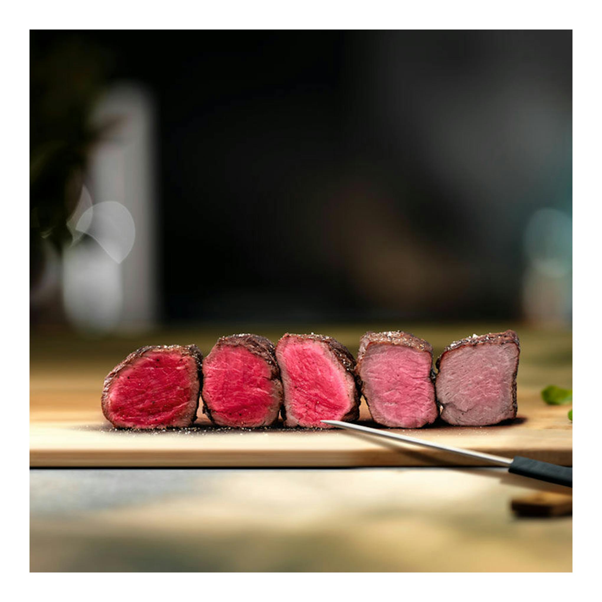 Filetes de carne roja en rodajas sobre una tabla de madera, con un cuchillo en primer plano.