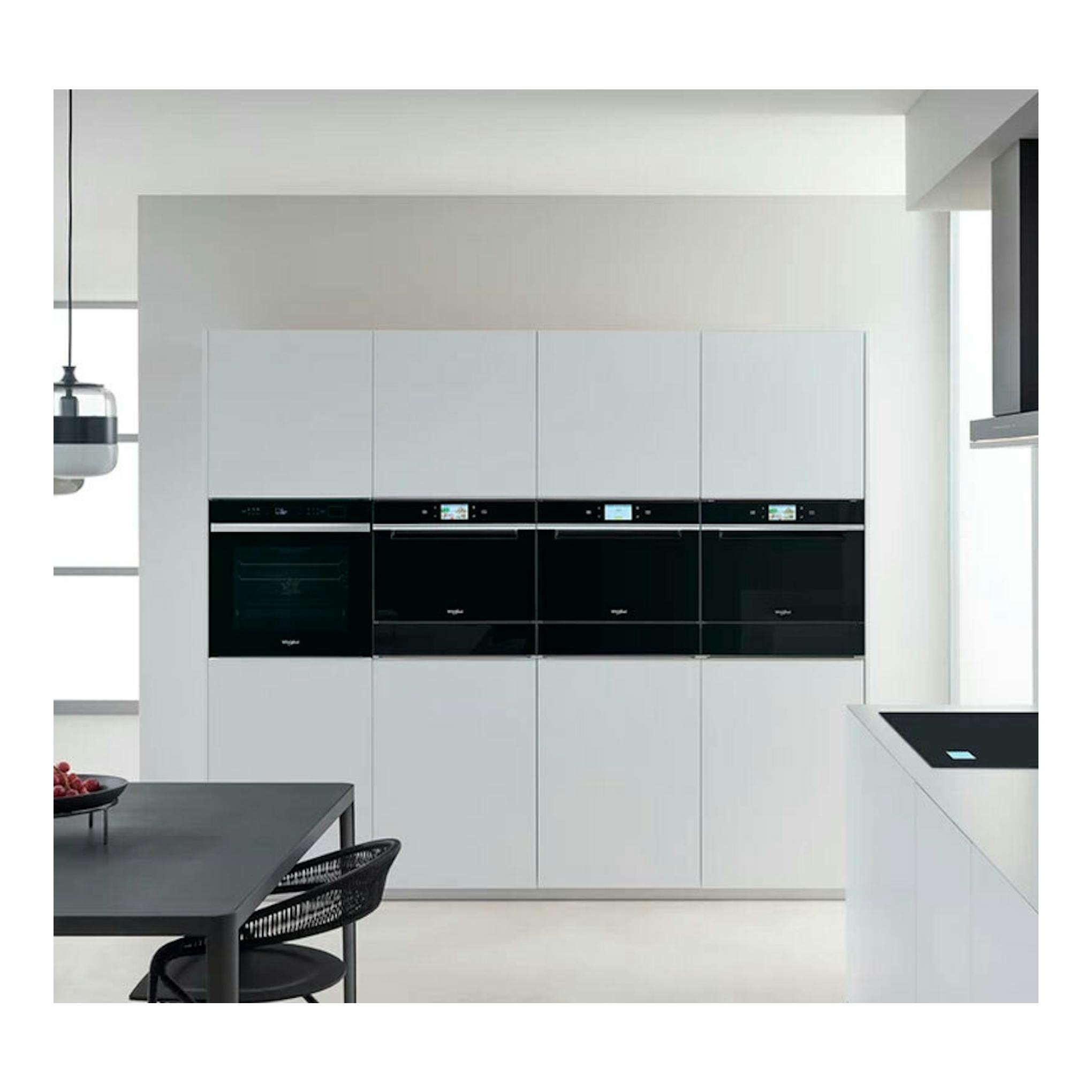 Horno Whirlpool W6 OS4 4S1 H BL de cristal negro, empotrado en cocina blanca, vista frontal.
