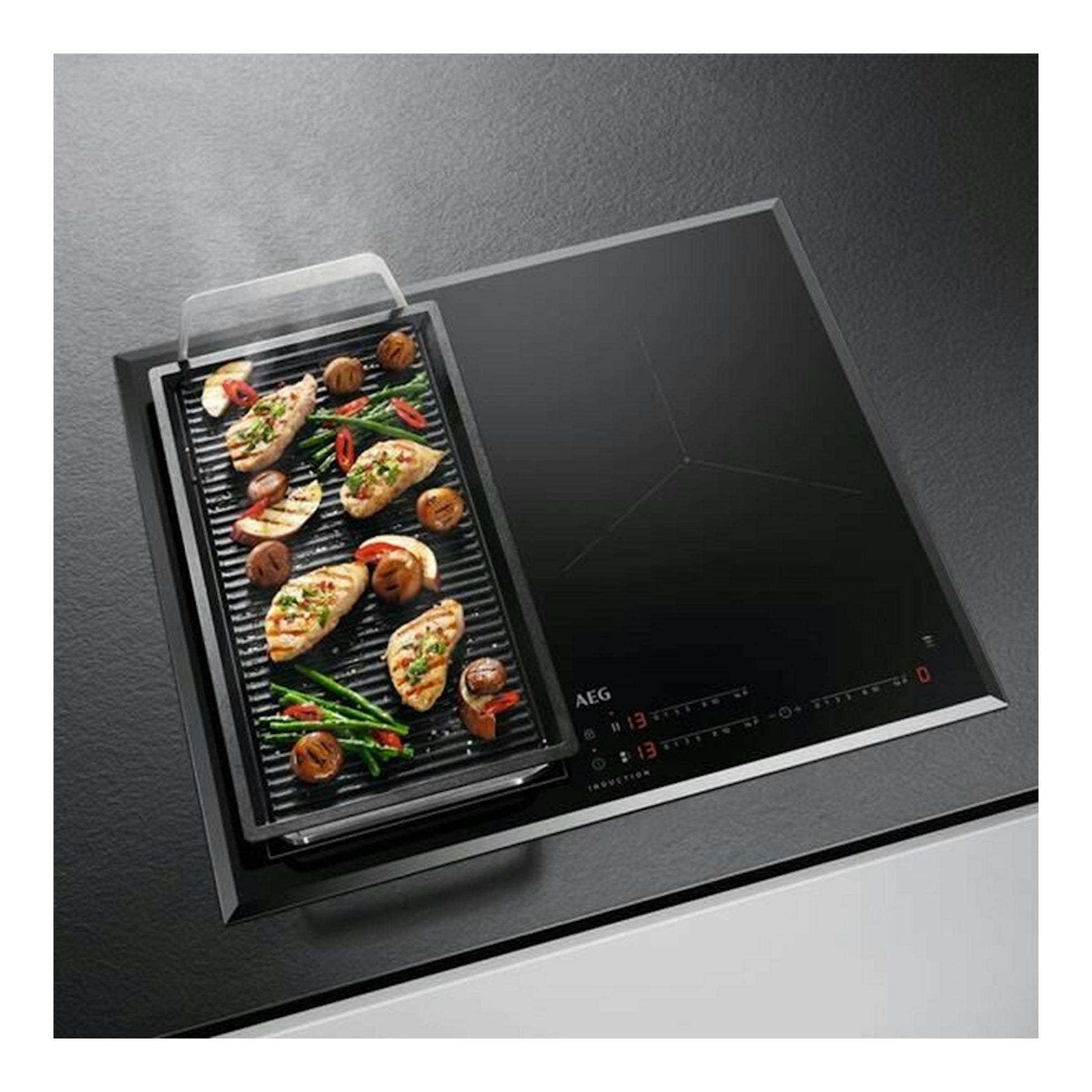 AEG ILB63445FB, placa de inducción negra en vista superior inclinada con bandeja grill y alimentos.