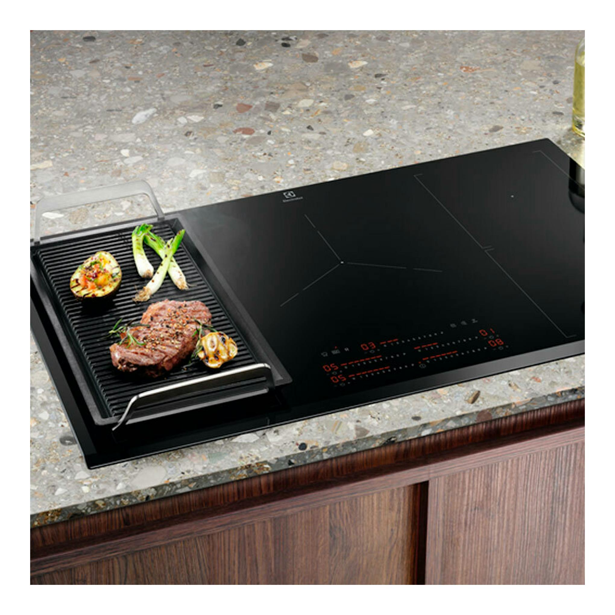 Placa de inducción Electrolux EIV95550 negra de 90 cm, vista en ángulo sobre encimera, con sartén grill.