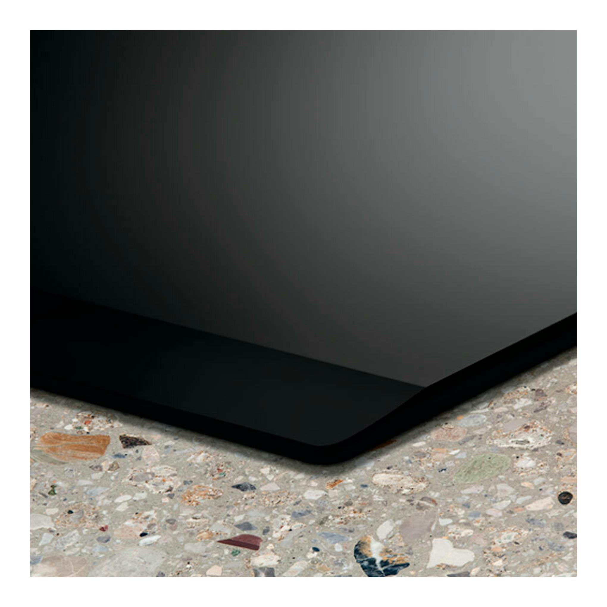 Detalle de la placa de inducción Electrolux EIV95550 negra, vista en esquina sobre encimera de terrazo.
